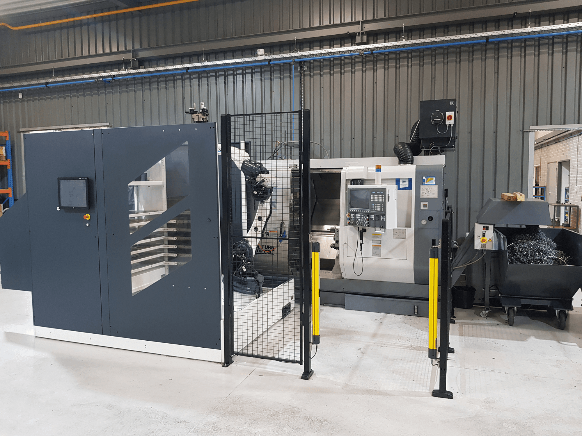 Torno automatizado ALTURN y máquina CNC mostrados en un entorno de fábrica; vista frontal con el panel de control y la valla de seguridad visibles.