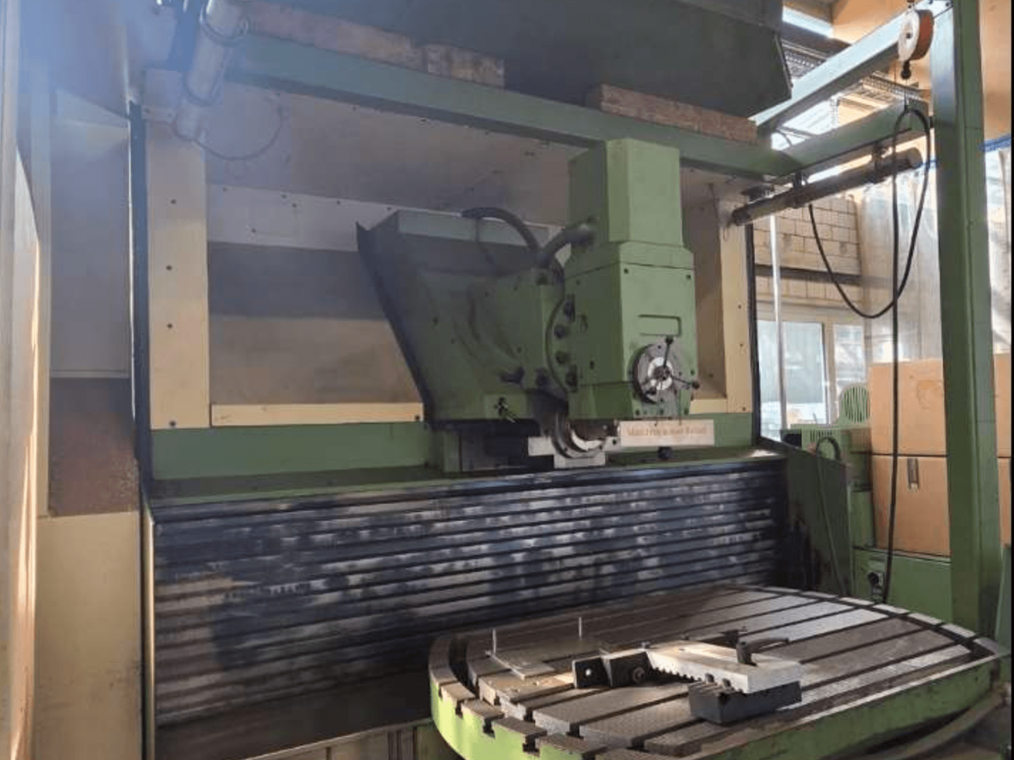 Centro de mecanizado universal MAHO MH1000 C en vista frontal, mostrando la estructura en verde, el husillo y la mesa giratoria con una pieza de trabajo.