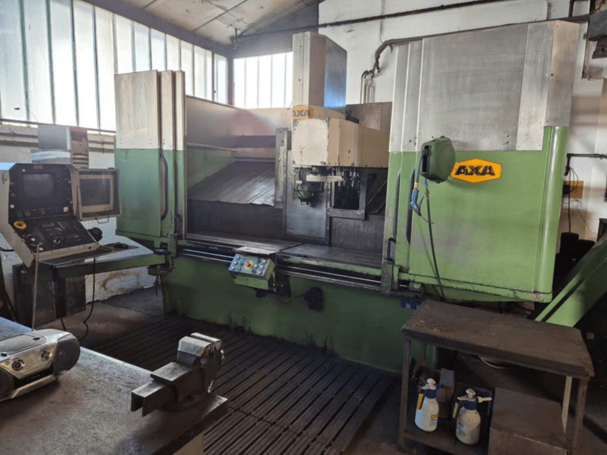 Centro de mecanizado vertical AXA VSC-2M, vista frontal, con panel de control y zona de trabajo con herramientas de corte y material de limpieza.