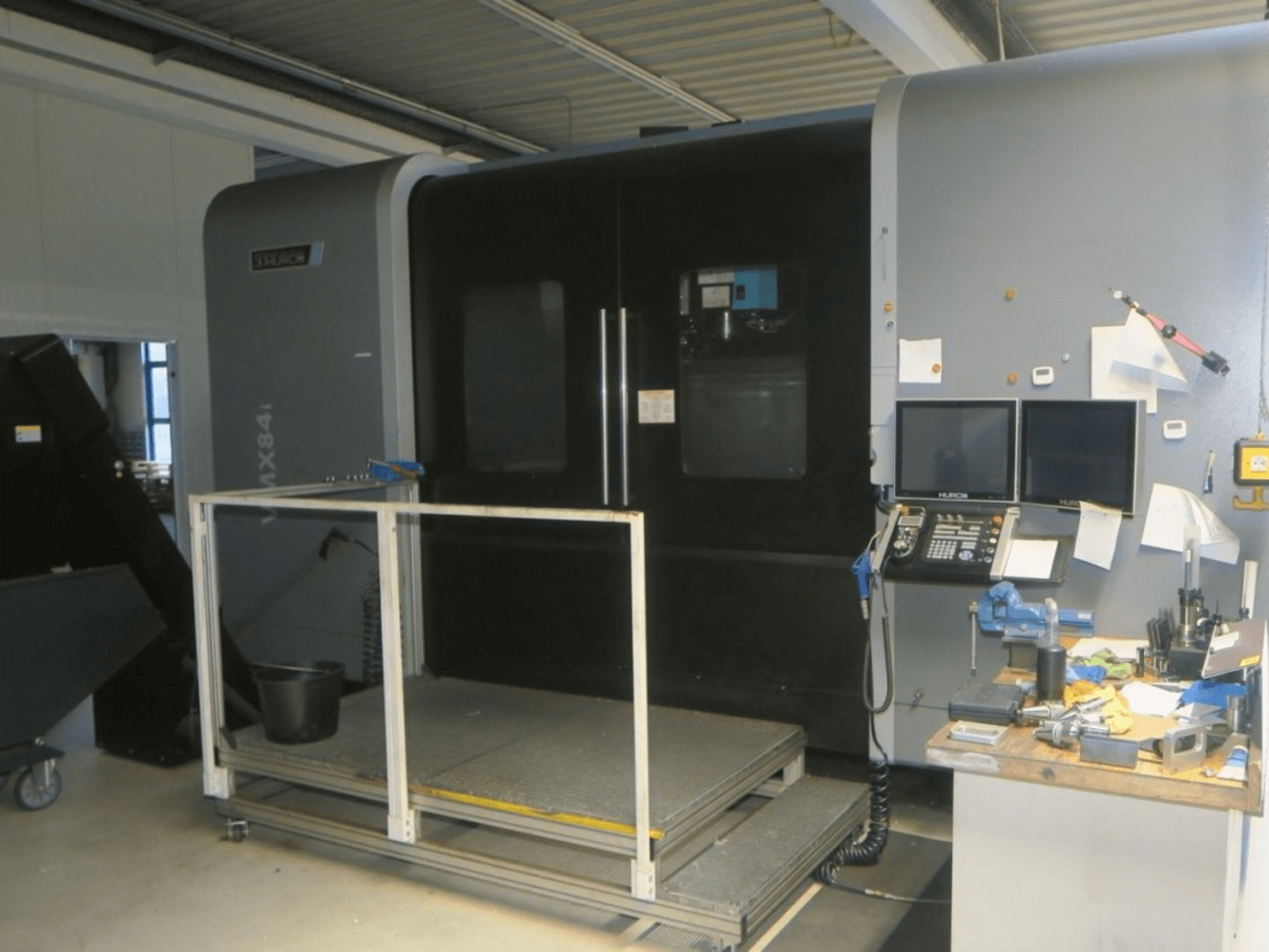 Máquina CNC Hurco MX84 en vista frontal, mostrando monitores duales, panel de control y espacio de trabajo con varias herramientas.