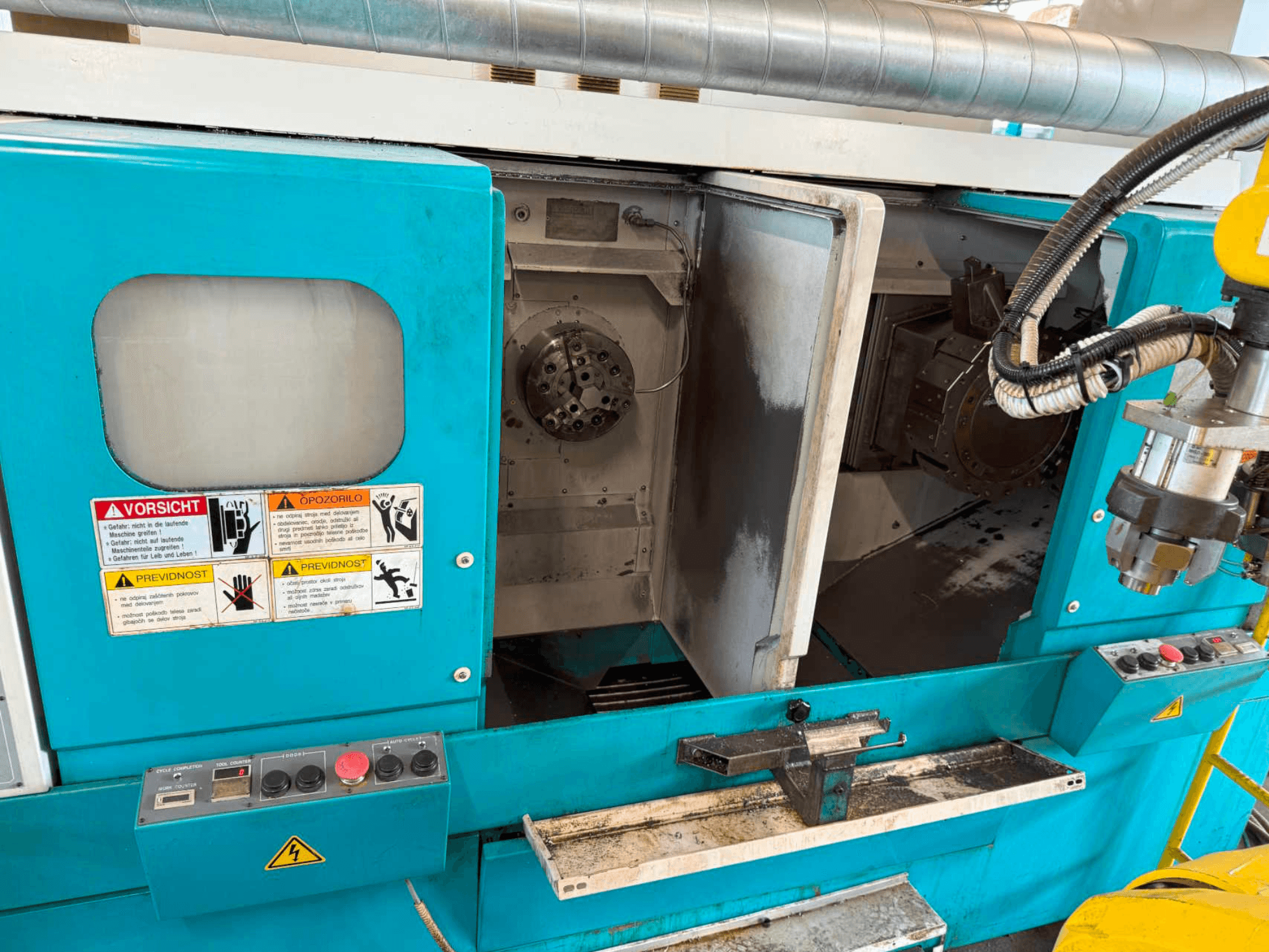 Máquina de torneado horizontal DOOSAN H310T, vista frontal mostrando el panel de control y la zona del husillo con advertencias de seguridad.