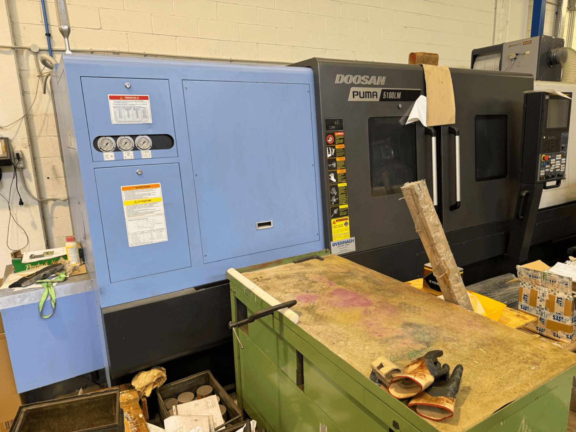 Máquina CNC Doosan Puma 5100LM y panel de control, vista lateral. Indicadores y etiquetas de advertencia visibles en la unidad de control azul.