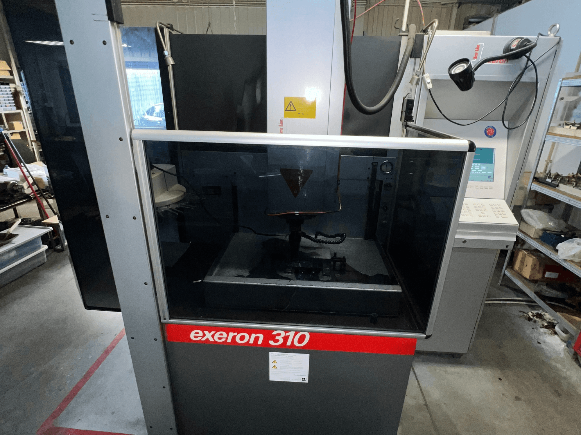 Vista frontal de una máquina Exeron 310, que muestra una cámara de cristal y un panel de control junto a las estanterías de la estación de trabajo.