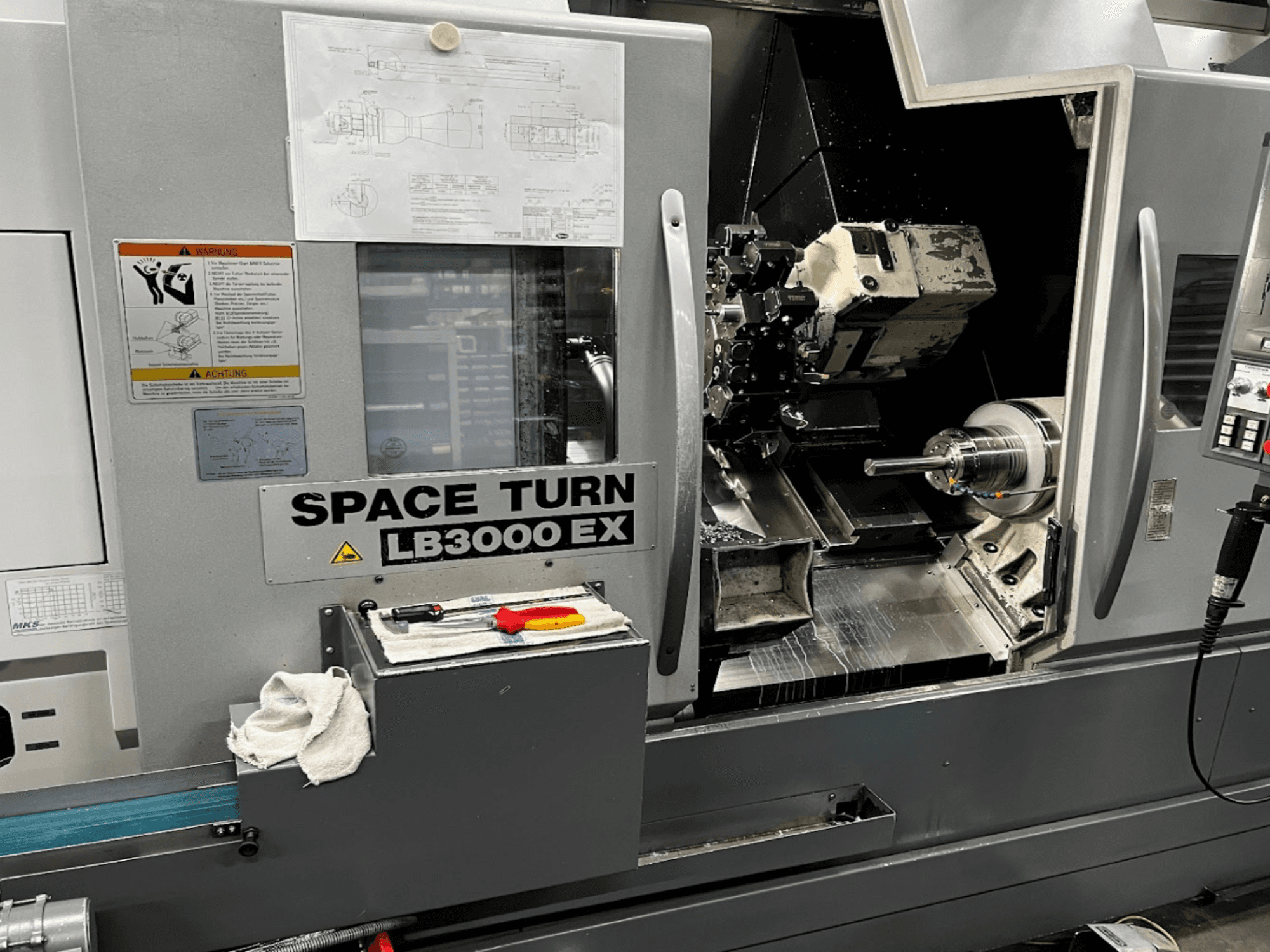 Máquina de torneado horizontal Okuma LB3000EX MYW, vista frontal con panel de control, herramientas y detalles del espacio de trabajo visibles.