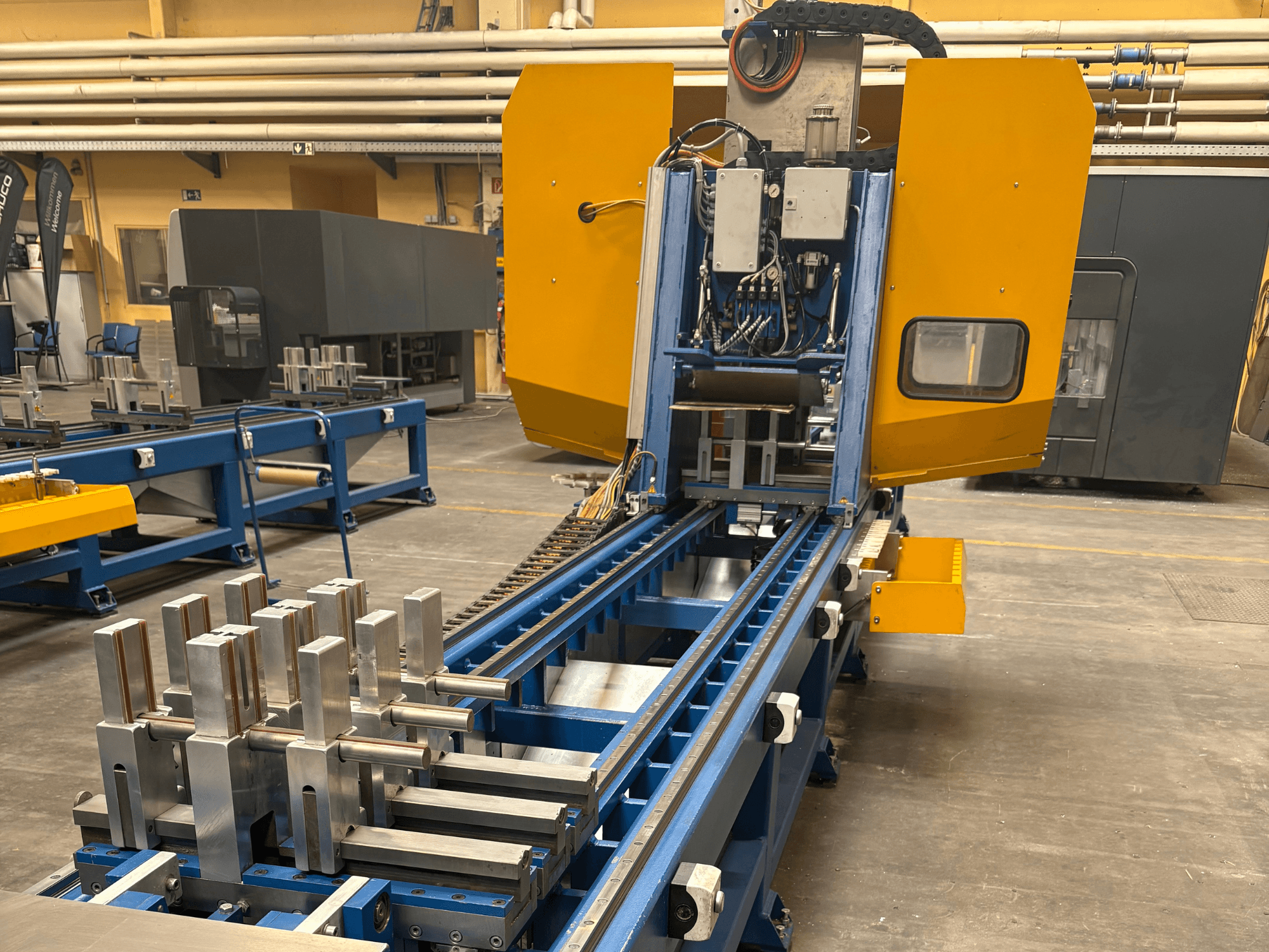 Vista frontal del Centro de Mecanizado Universal SCHÜCO PBX AL, mostrando piezas metálicas en una bancada de mecanizado azul.