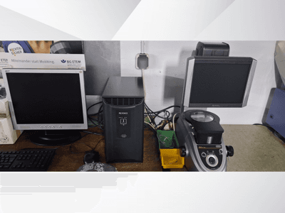 Dos monitores de ordenador, uno Acer y otro Keyence, junto a un dispositivo negro y un microscopio, vistos de frente.