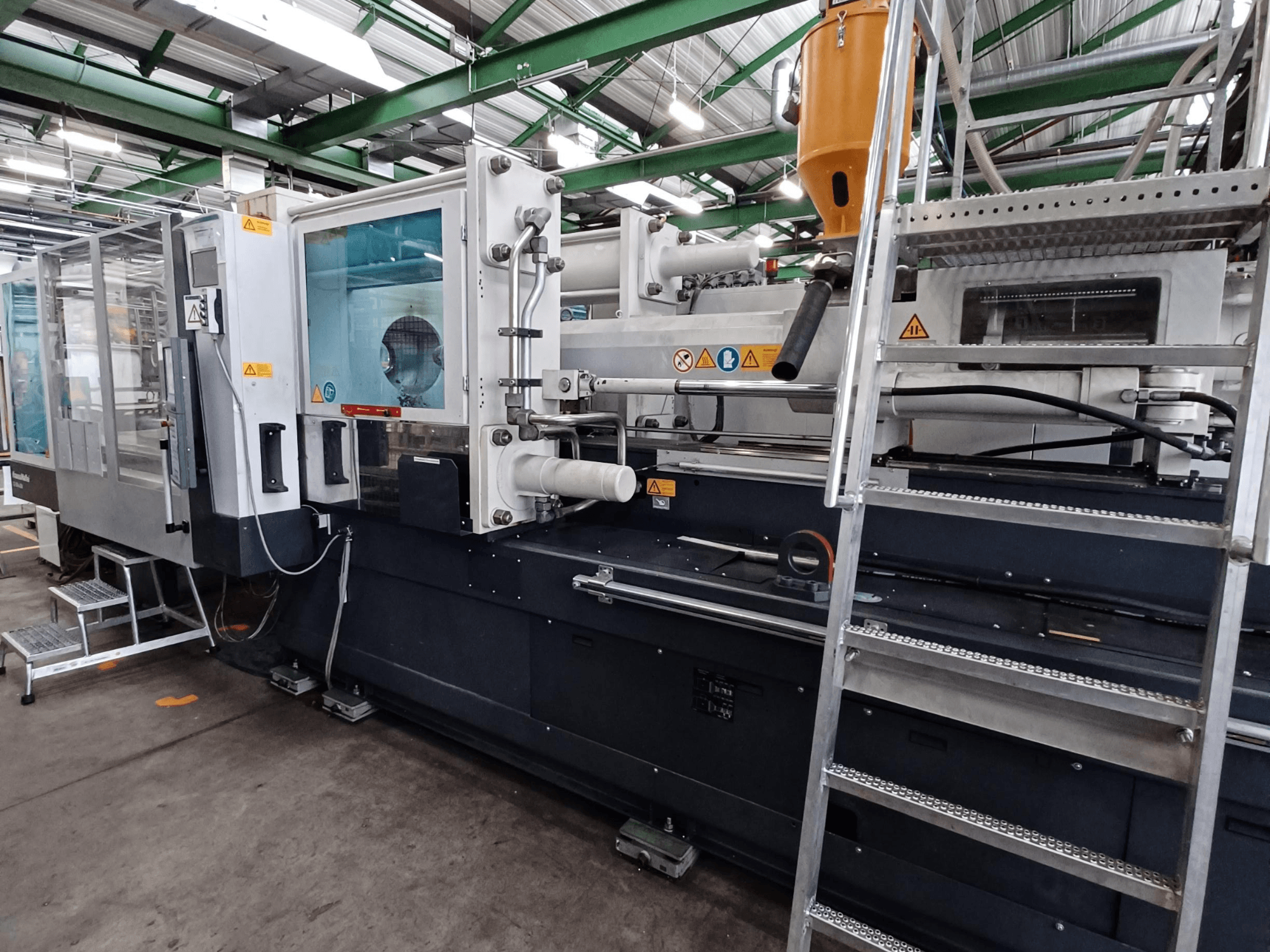 Industrial injection molding machine with a clear front view, showing brand markings, control panel, and material hopper.