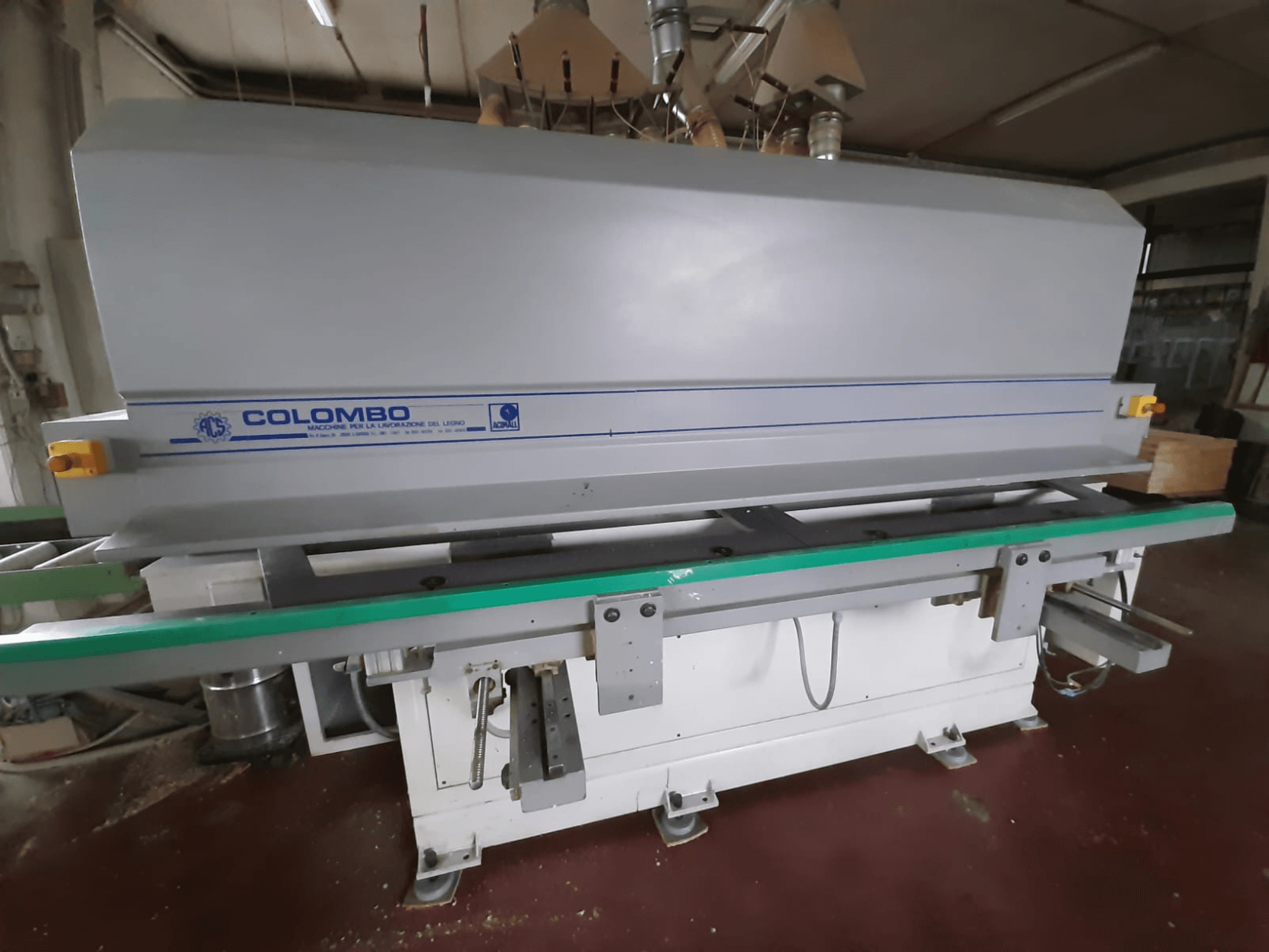Máquina de procesamiento de madera Colombo, vista frontal, con una larga mesa verde, botones de control y un cuerpo gris con detalles azules.