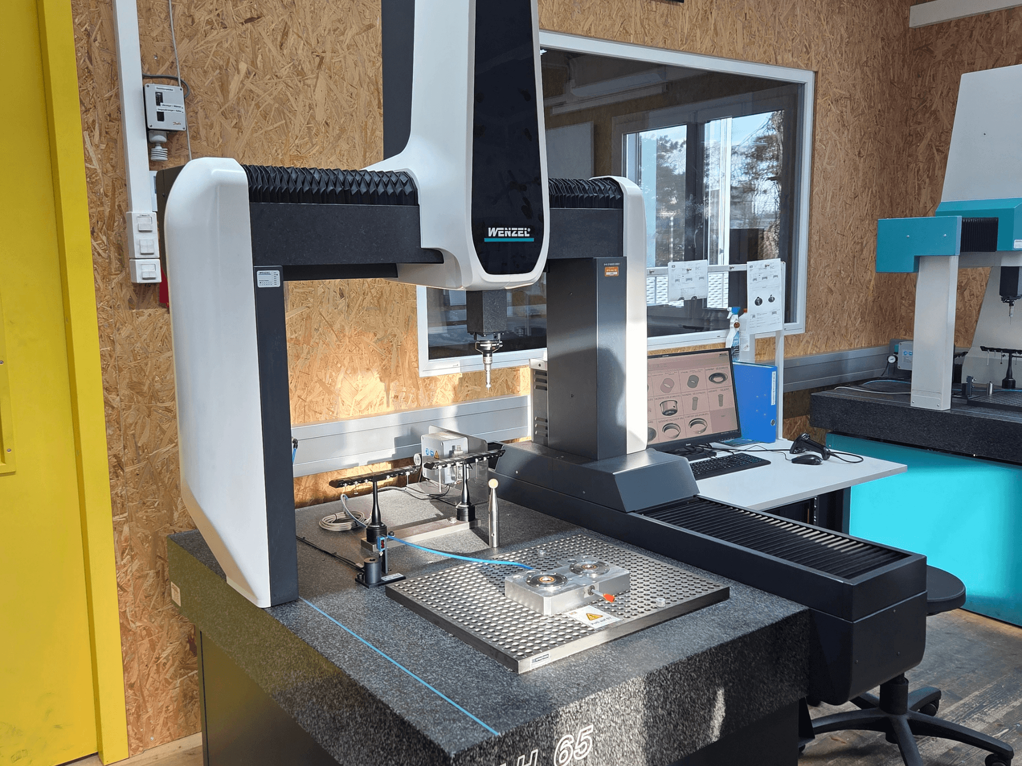 Máquina de medición por coordenadas Wenzel LH 65 en una configuración de laboratorio, vista frontal, mostrando herramientas de medición y un monitor.