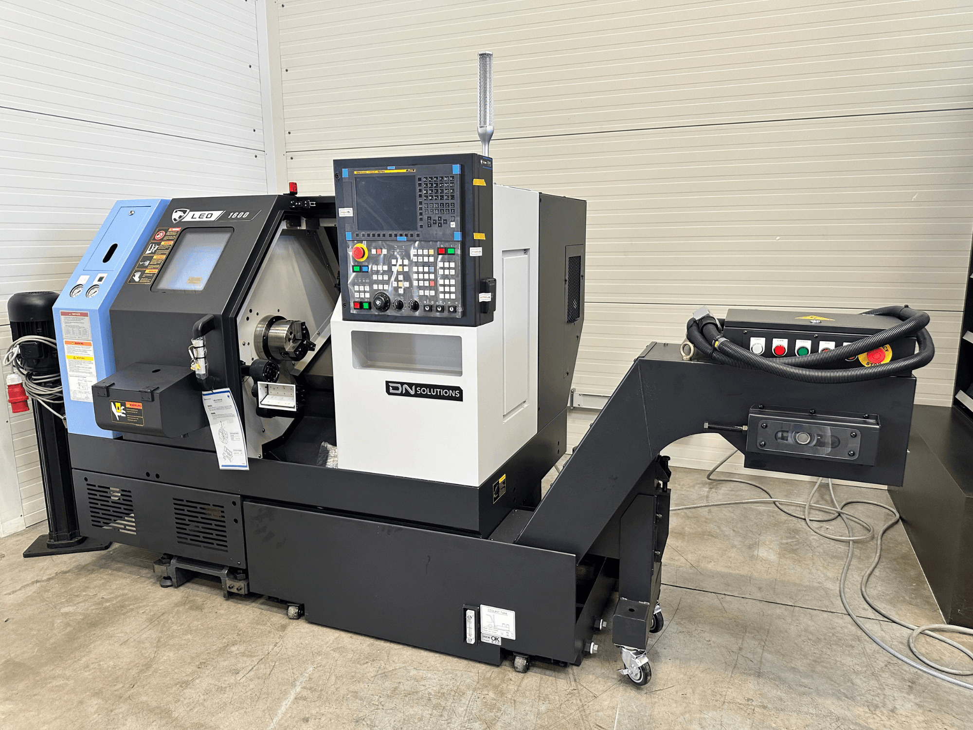 Vista frontal del centro de torneado y fresado DN SOLUTIONS Leo 1600, con panel de control digital y portaherramientas, sobre una base negra.