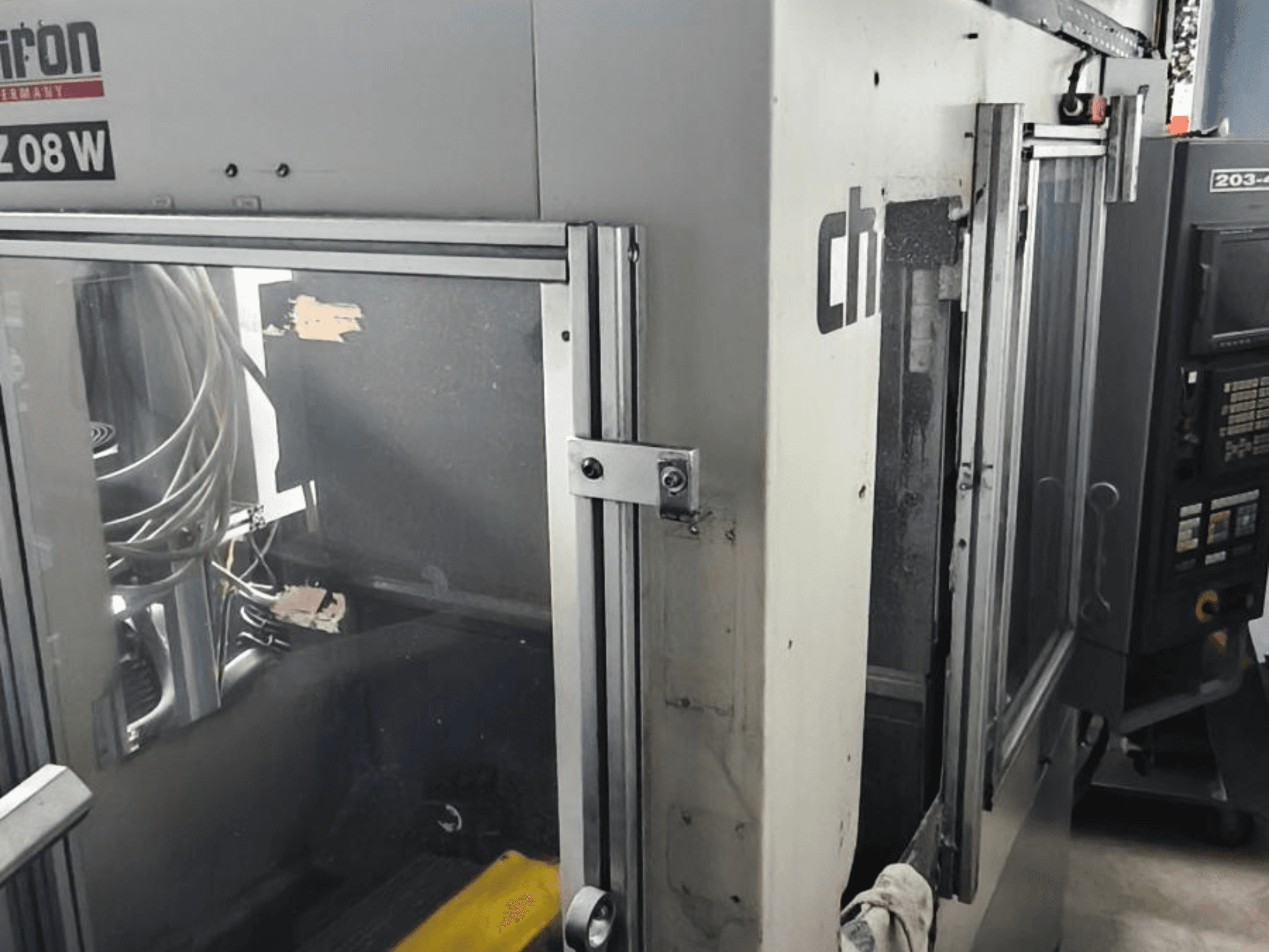 Centro de mecanizado vertical CHIRON FZ 08 W, vista frontal mostrando el panel de control y las puertas parcialmente abiertas, con componentes internos visibles.