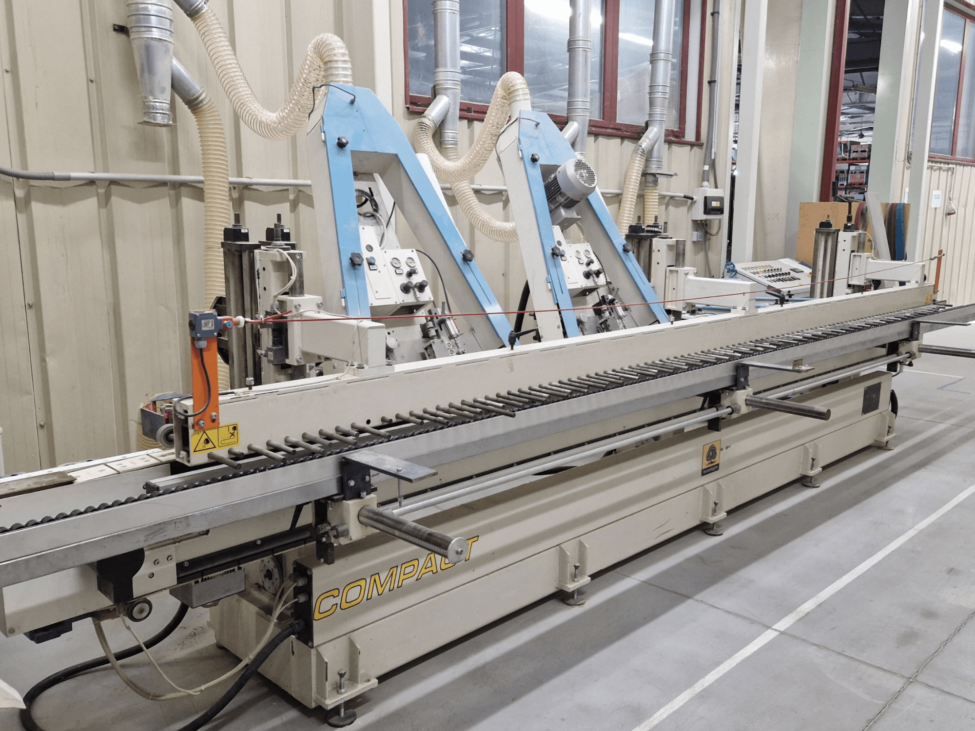 Lijadora de banda TECNOLEGNO COMPACT 52 en un taller, mostrando el panel de control y el mecanismo de la banda de lijado desde una vista lateral.