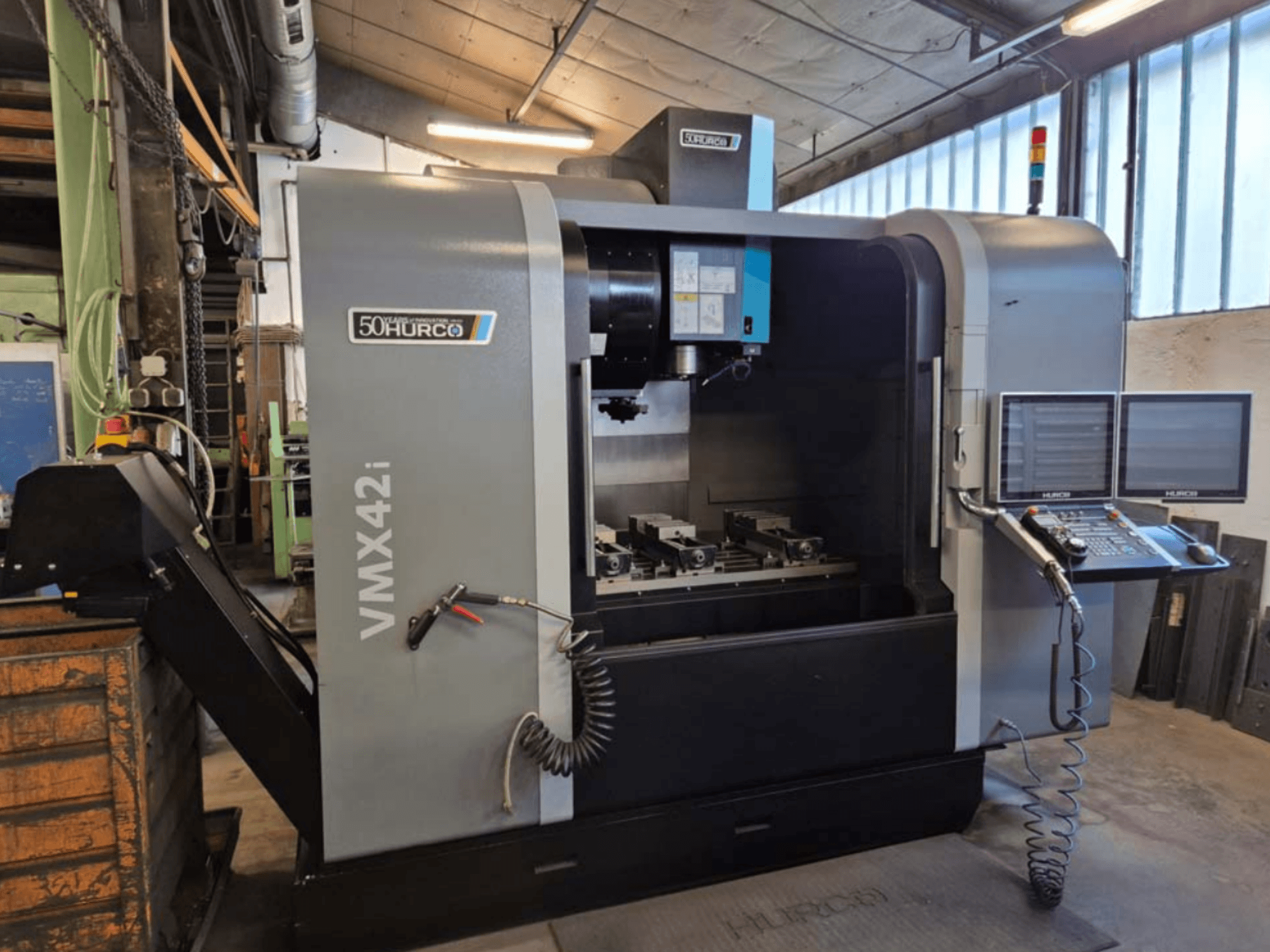 Centro de mecanizado vertical Hurco VMX 42i, vista frontal, mostrando el panel de control y el área de trabajo con mordazas.
