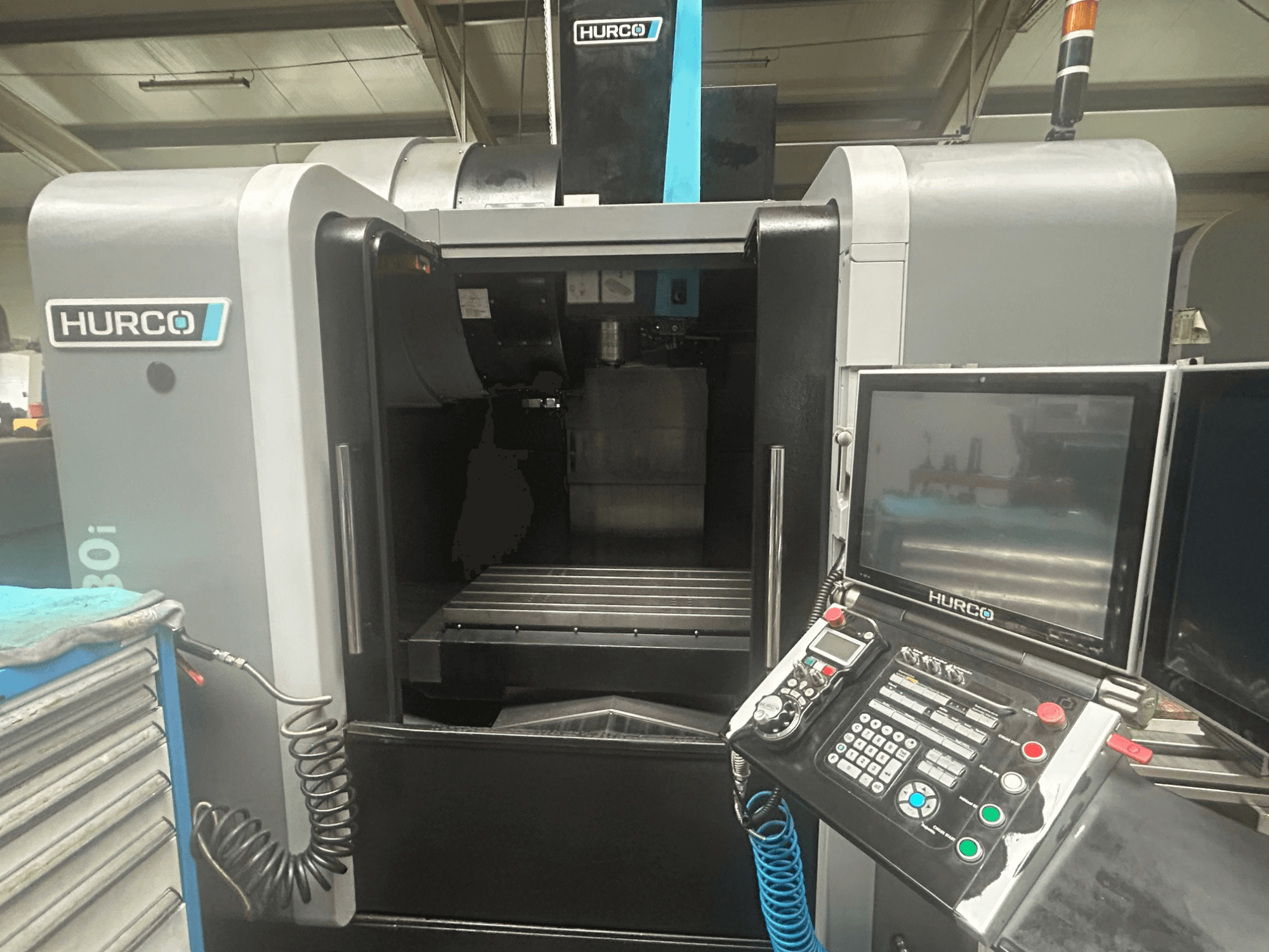 Vista frontal de la máquina CNC Hurco VM30i, con panel de control con botones, pantalla y área de almacenamiento de herramientas.