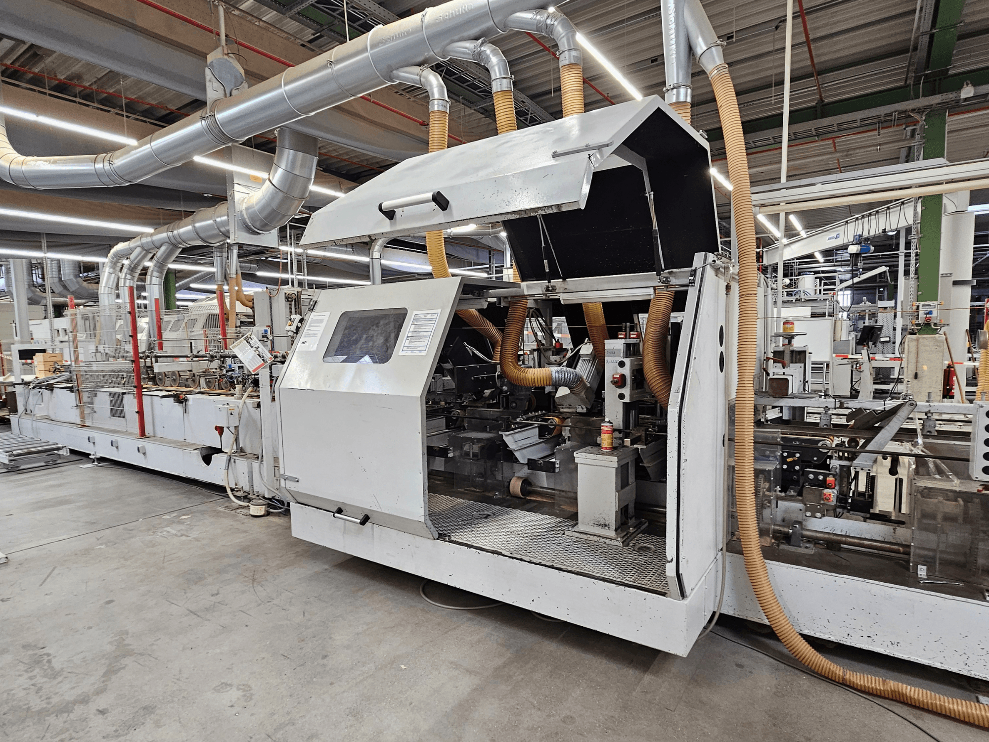 Chapadora de cantos HOMAG FG63 en fábrica, vista lateral mostrando los componentes operativos y el sistema de extracción de polvo.