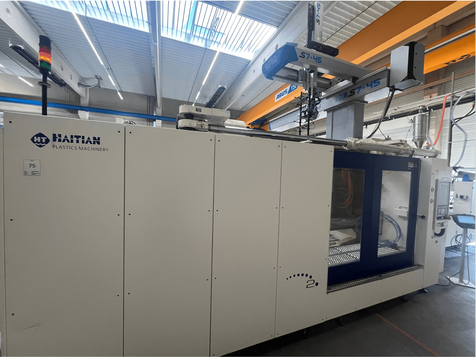 Máquina de moldeo por inyección Haitian S7-45 en vista lateral con panel de control e indicador luminoso de seguridad. Diseño en blanco y azul.