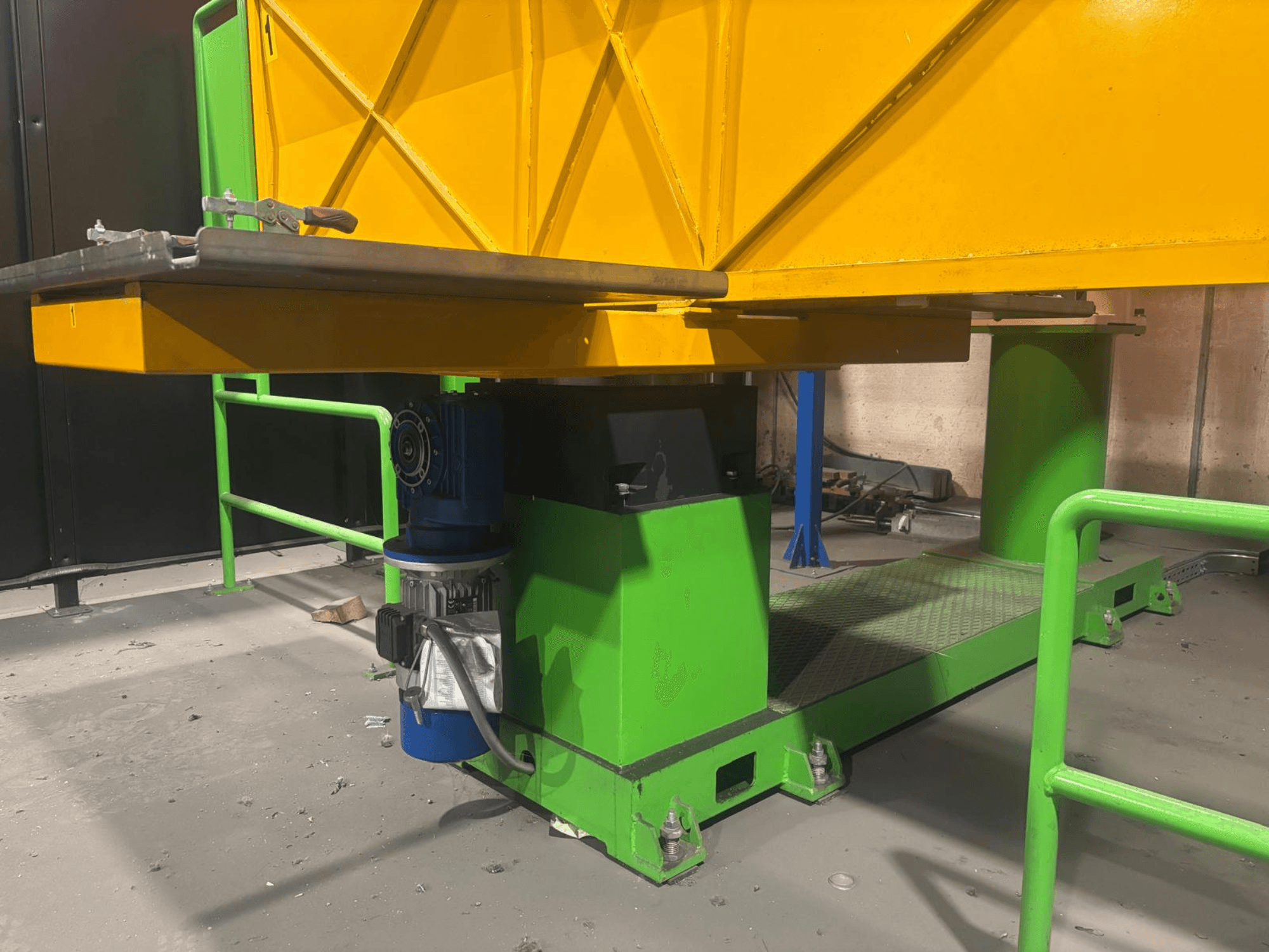 Green and yellow industrial machinery from a low front view, featuring a motor and platform with a textured surface.