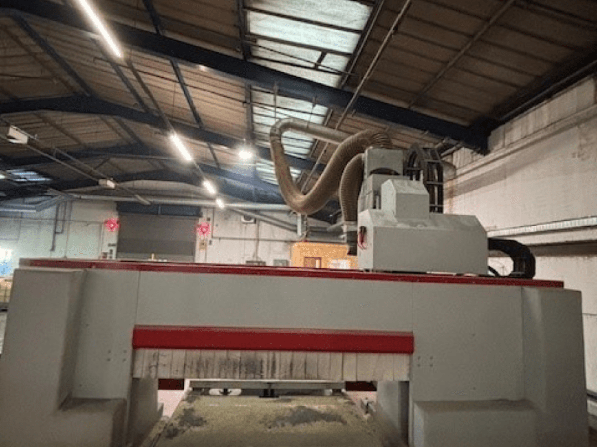 Fresadora CNC en un taller, vista lateral destacando el diseño rojo y gris, sistema de extracción de polvo acoplado.