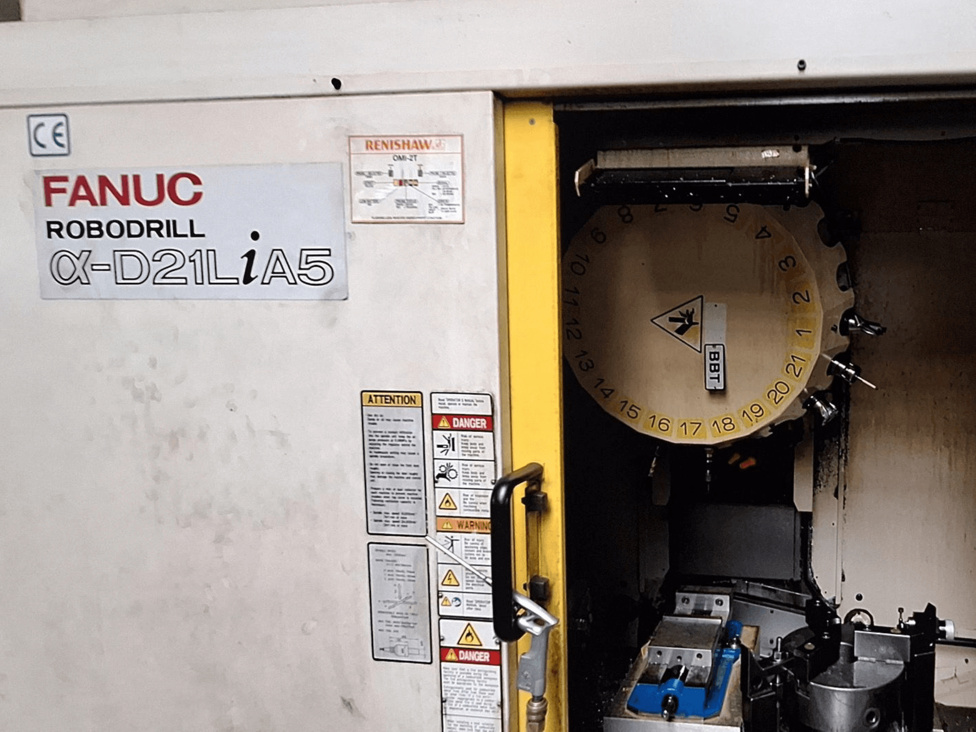 FANUC Robodrill α-D21LiA5, front view. Shows tool carousel and machining area with clamps and warnings on the door.