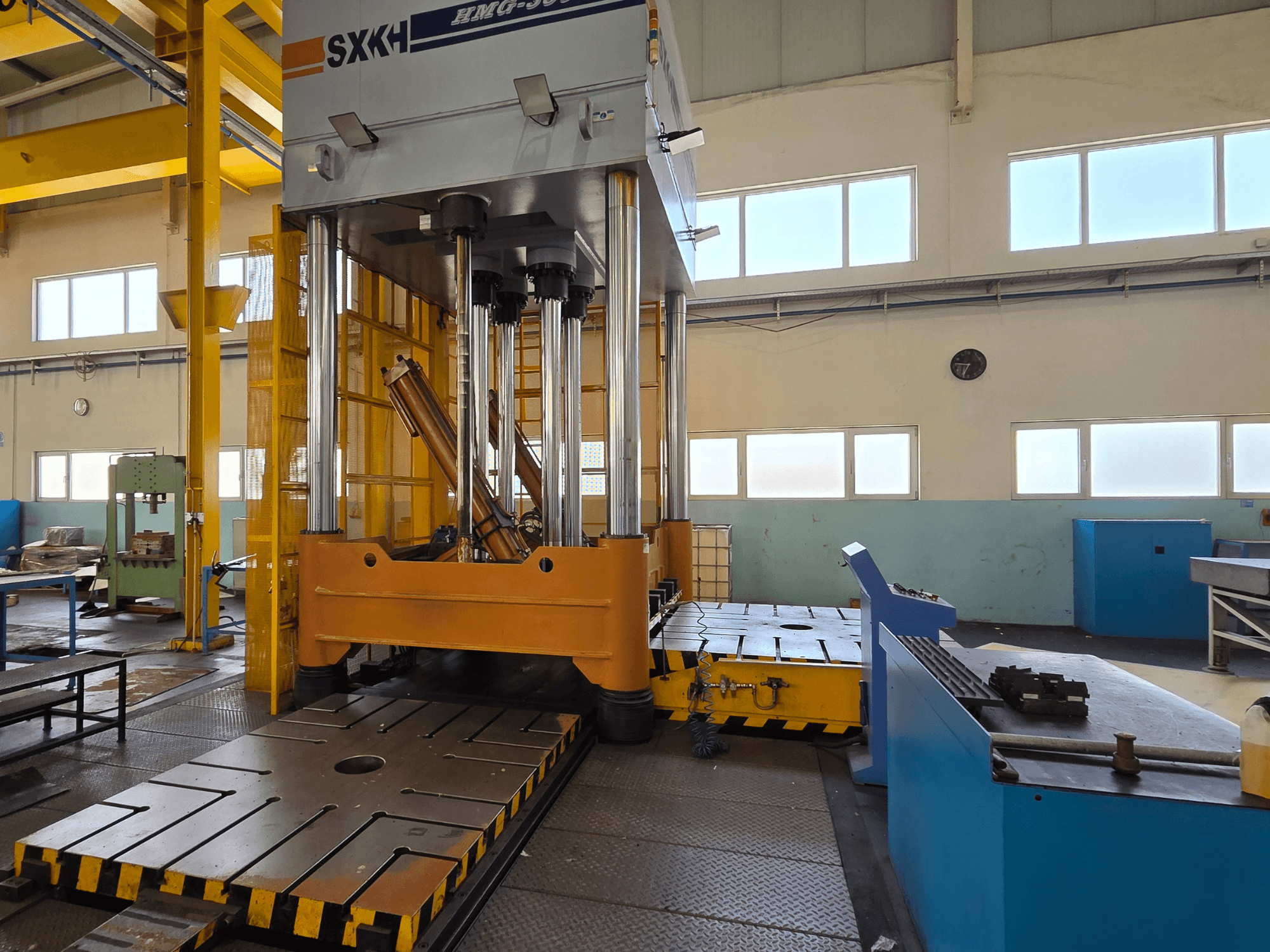 Vista frontal de la prensa hidráulica SXKH HMG-300JM, con grandes cilindros de prensado y una base robusta en una fábrica.