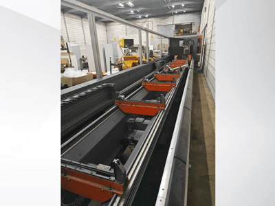 Vista lateral de máquina CNC industrial, con guías lineales, pinzas naranjas y componentes de precisión en un entorno de almacén.