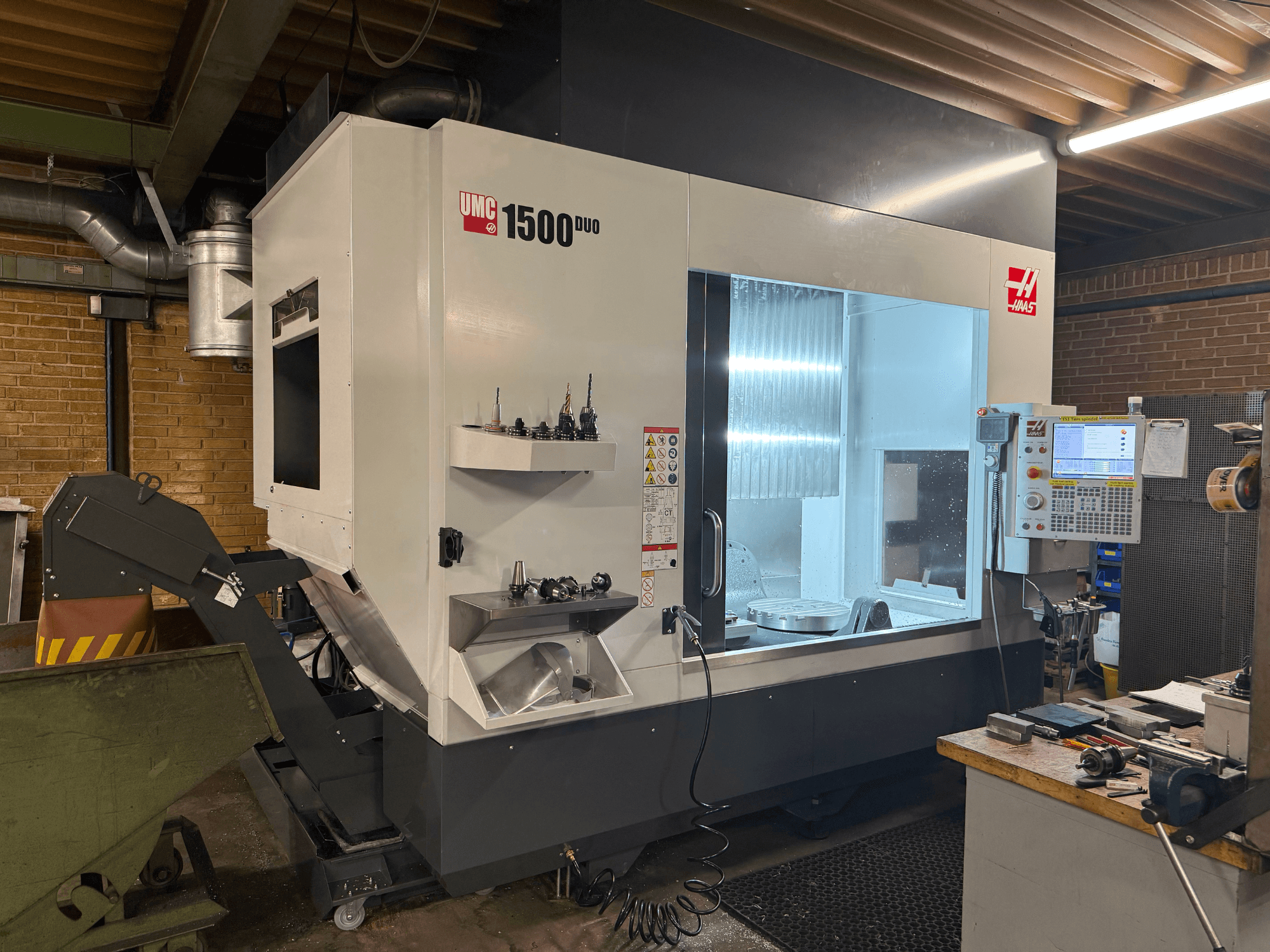 Haas UMC 1500DUO CNC machine, front view, features a large window, control panel, and tool holders on a shelf.