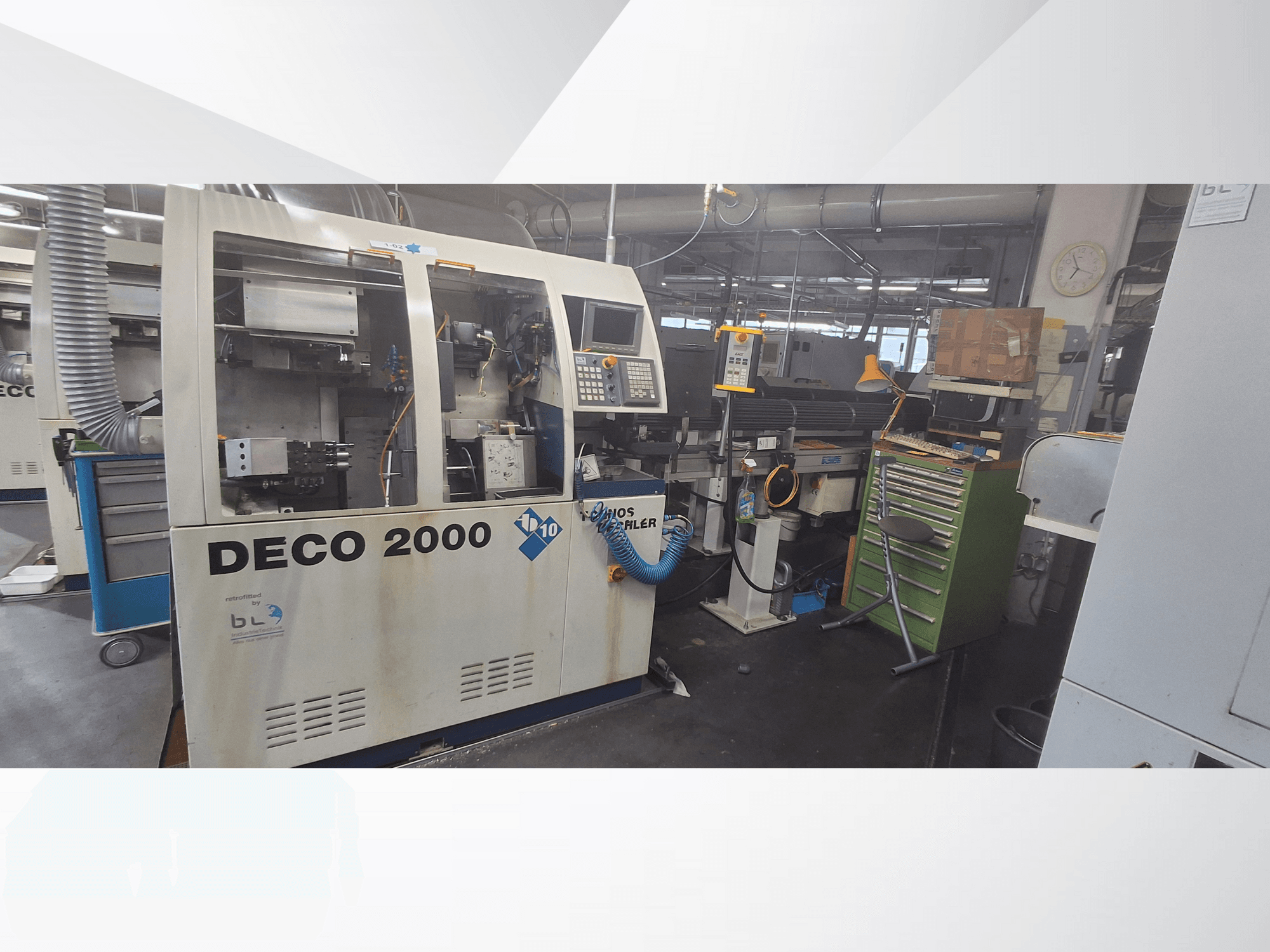 Máquina DECO 2000 vista de frente, con panel de control, tuberías y un espacio de trabajo desordenado con herramientas y cajas.