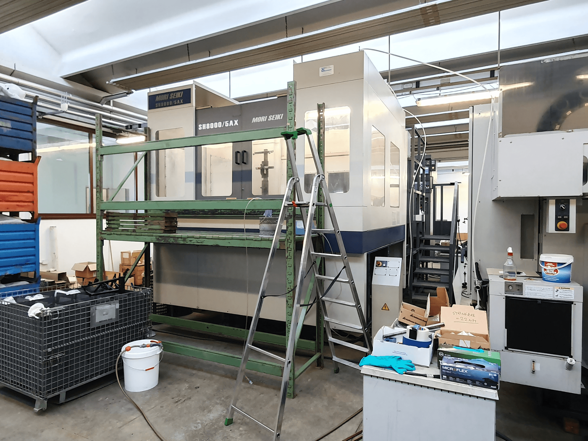 Máquina CNC Mori Seiki SH-8000/5AX en un taller, vista frontal, con herramientas de taller y cajas de almacenamiento cerca.