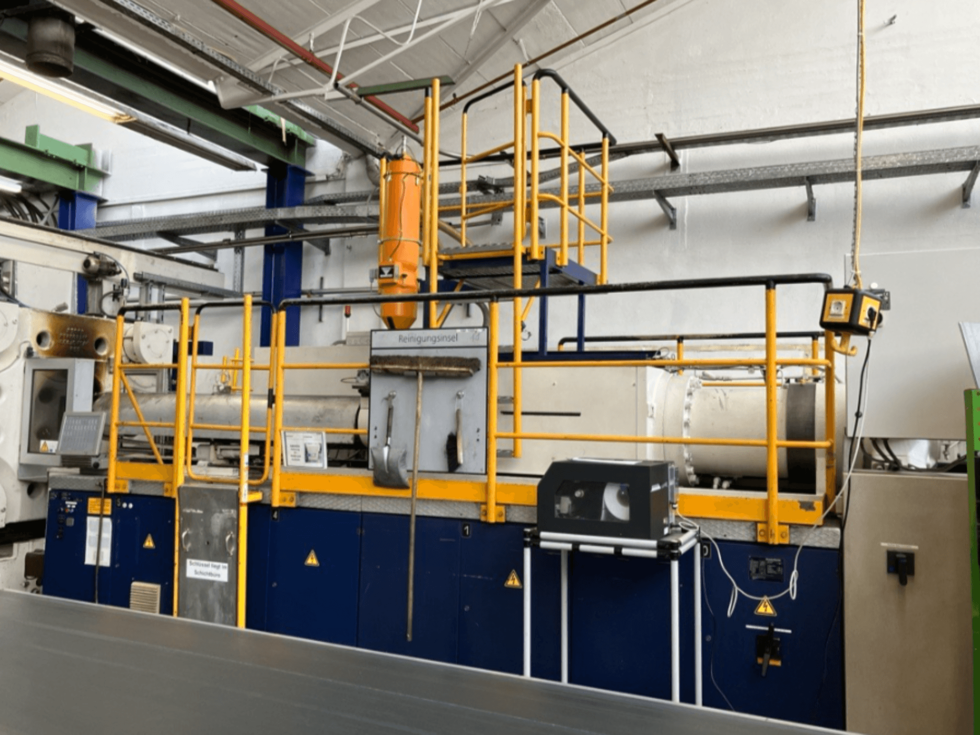 Máquina de moldeo por inyección hidráulica Krauss Maffei 1000-8000 M, vista lateral con barandilla de seguridad y panel de control visibles.