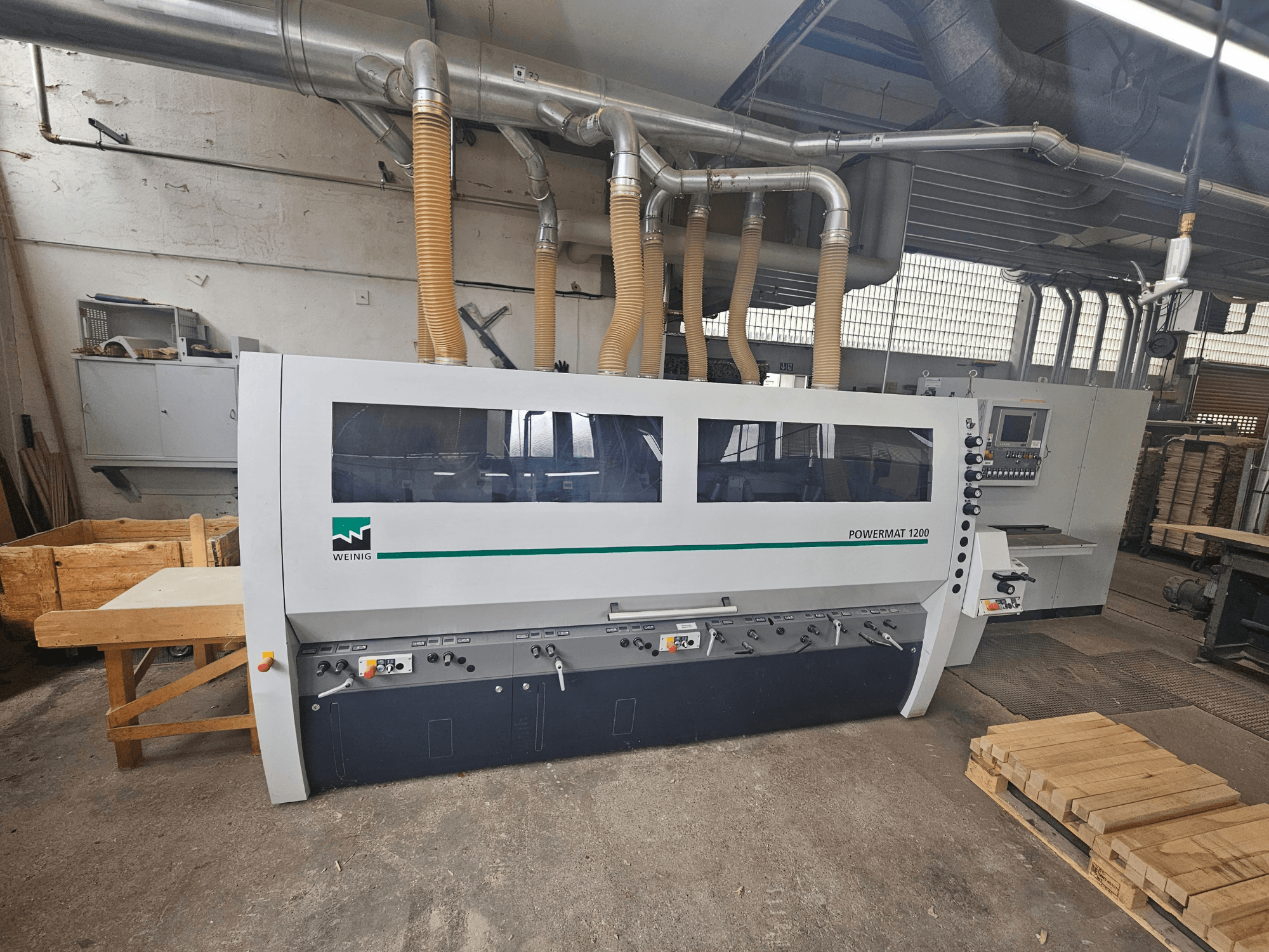 Máquina para trabajar la madera Weinig Powermat 1200, vista frontal, con panel de control y pilas de madera en un taller.