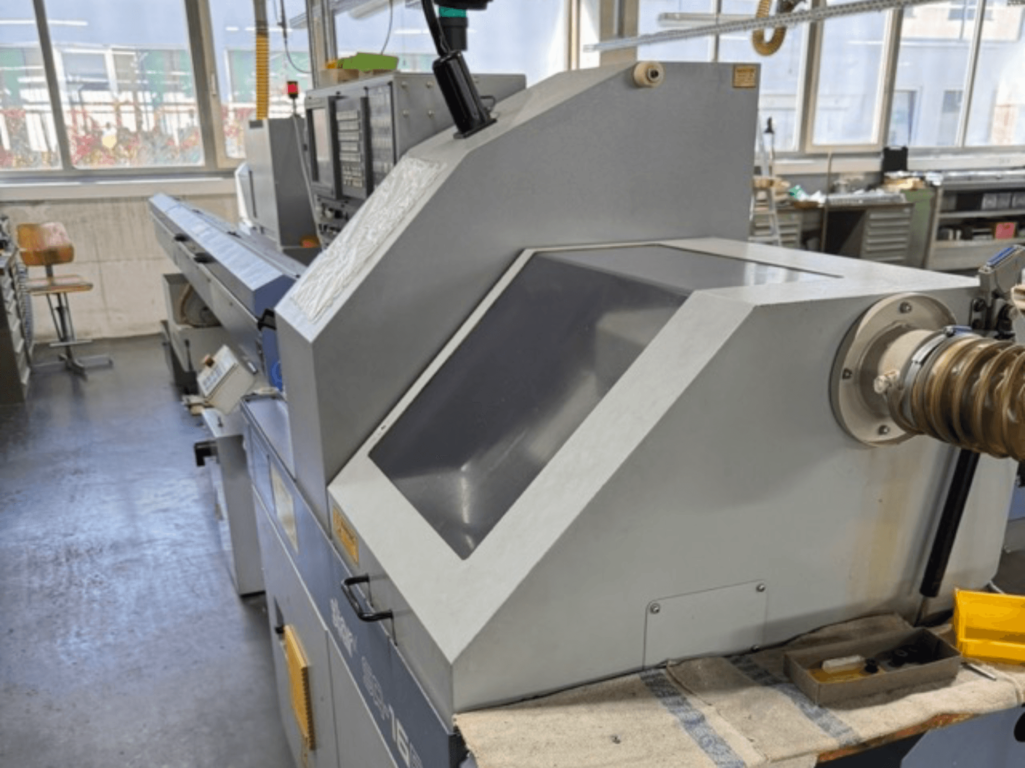 Máquina industrial gris vista desde el lateral, cuenta con un gran panel en ángulo, botones de control y un accesorio para la manguera.