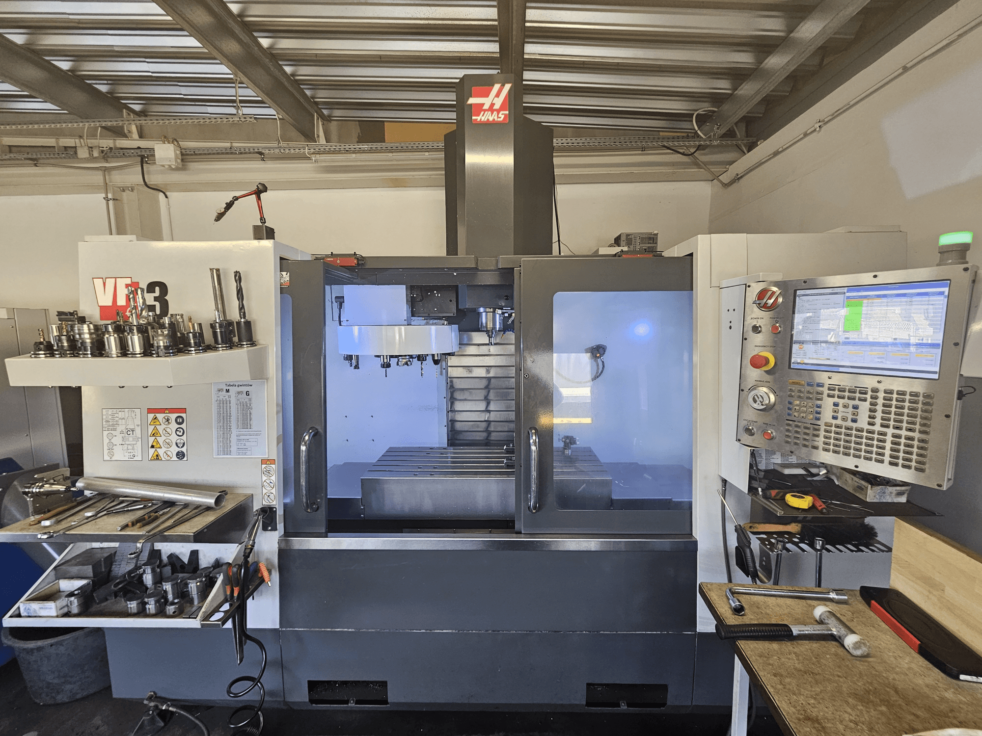 Máquina CNC Haas VF-3 en un taller, vista frontal que muestra las herramientas, los controles y la zona de fresado con el interior iluminado.