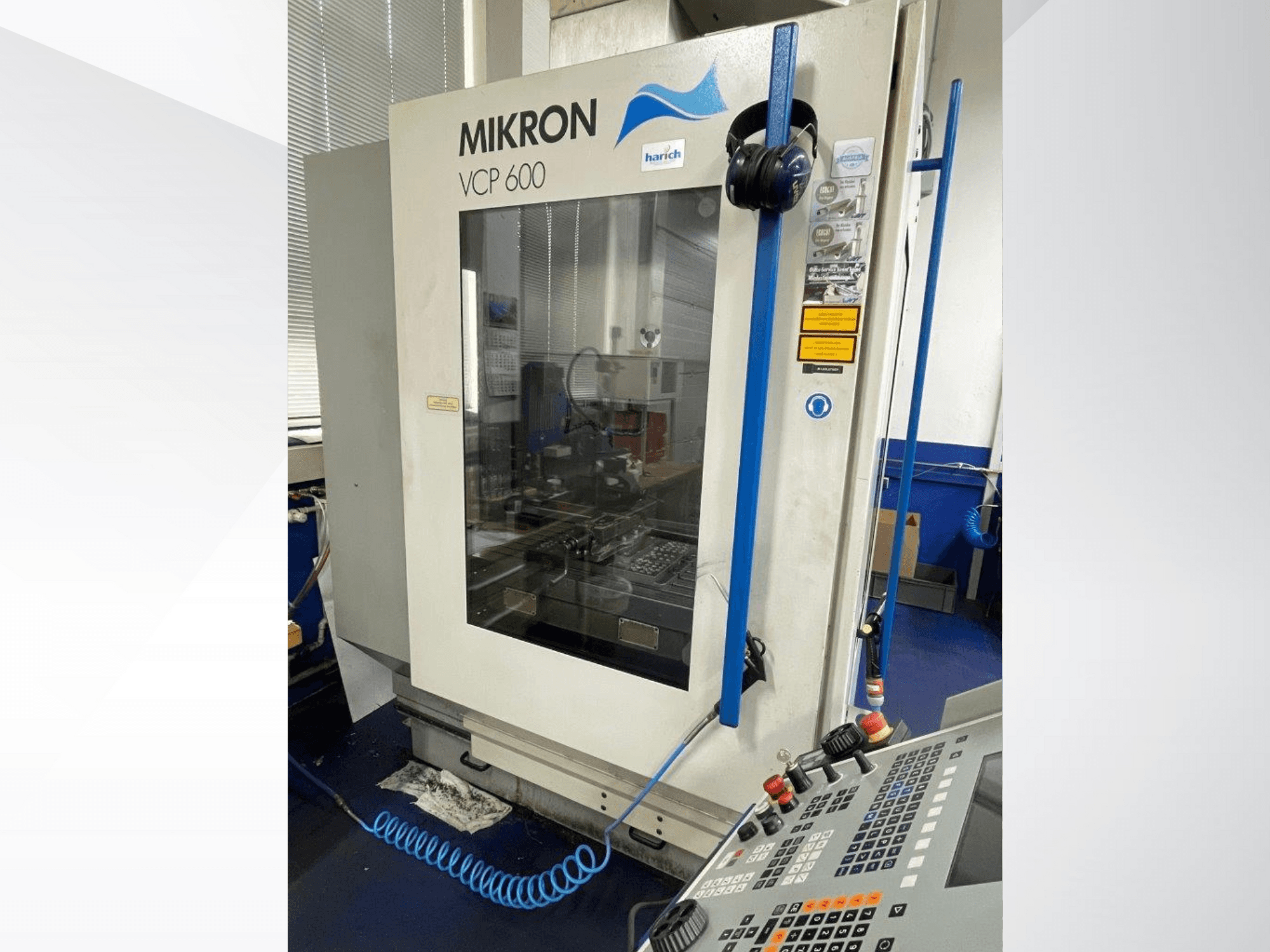 Máquina CNC Mikron VCP 600, vista frontal, presenta panel de control con botones y zona de mecanizado visible tras el cristal.