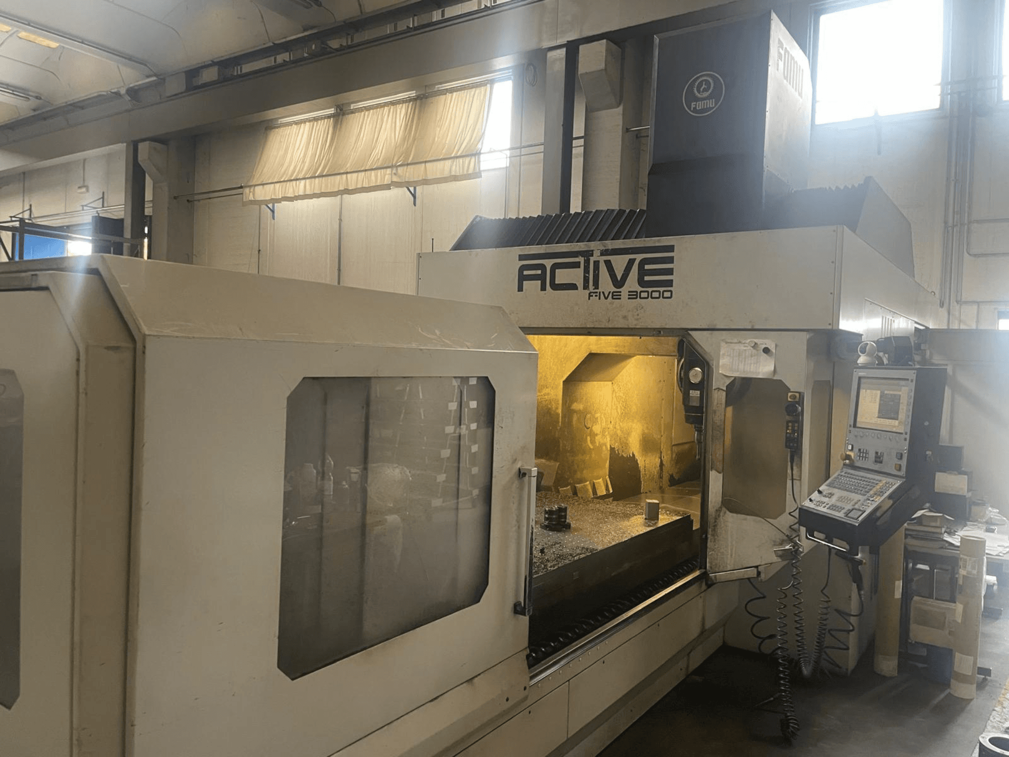 Vista frontal de la máquina CNC ACTIVE Five 3000, mostrando el panel de control y el área de trabajo con una pieza parcialmente mecanizada en el interior.