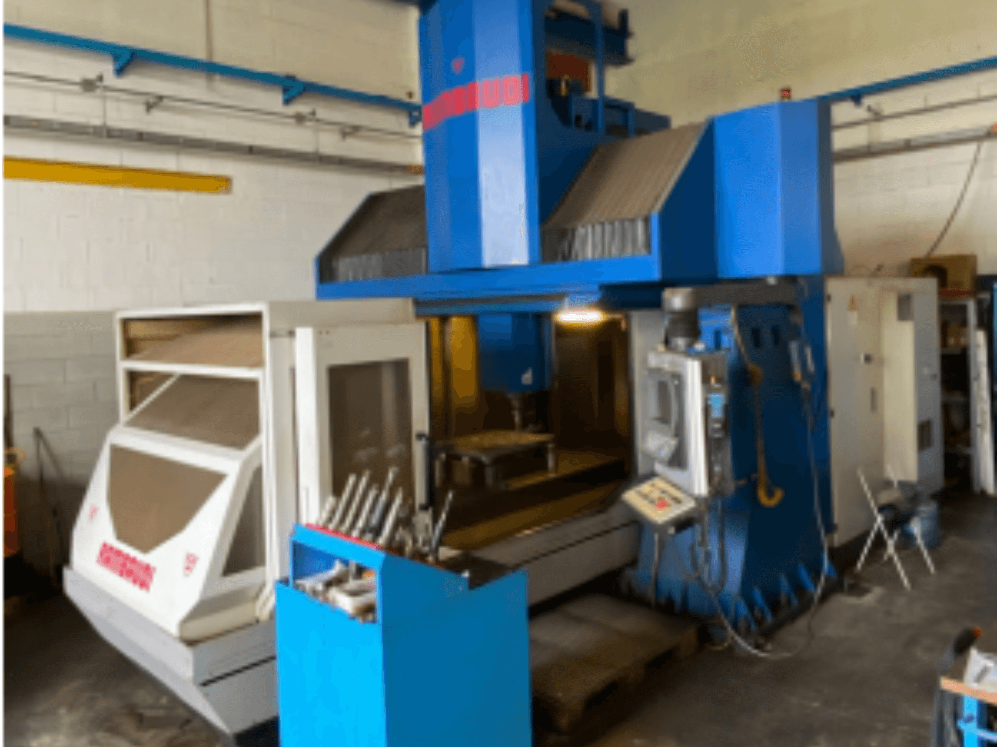 Centro de mecanizado vertical Rambaudi RF103, vista frontal mostrando controles, almacenamiento de herramientas y área de mecanizado. Exterior azul y blanco.