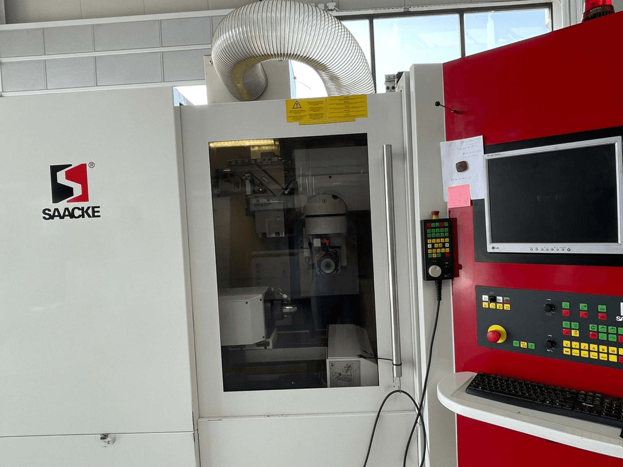 Máquina SAACKE en blanco y rojo, vista frontal, cuenta con un panel de control, monitor y partes internas visibles a través del cristal.