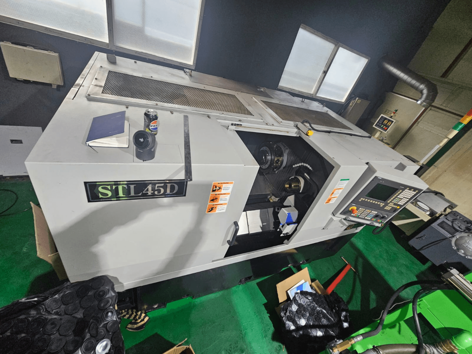 Máquina CNC STL45D vista desde arriba, mostrando el panel de control, la pieza cilíndrica, el portátil y la lata en la parte superior.