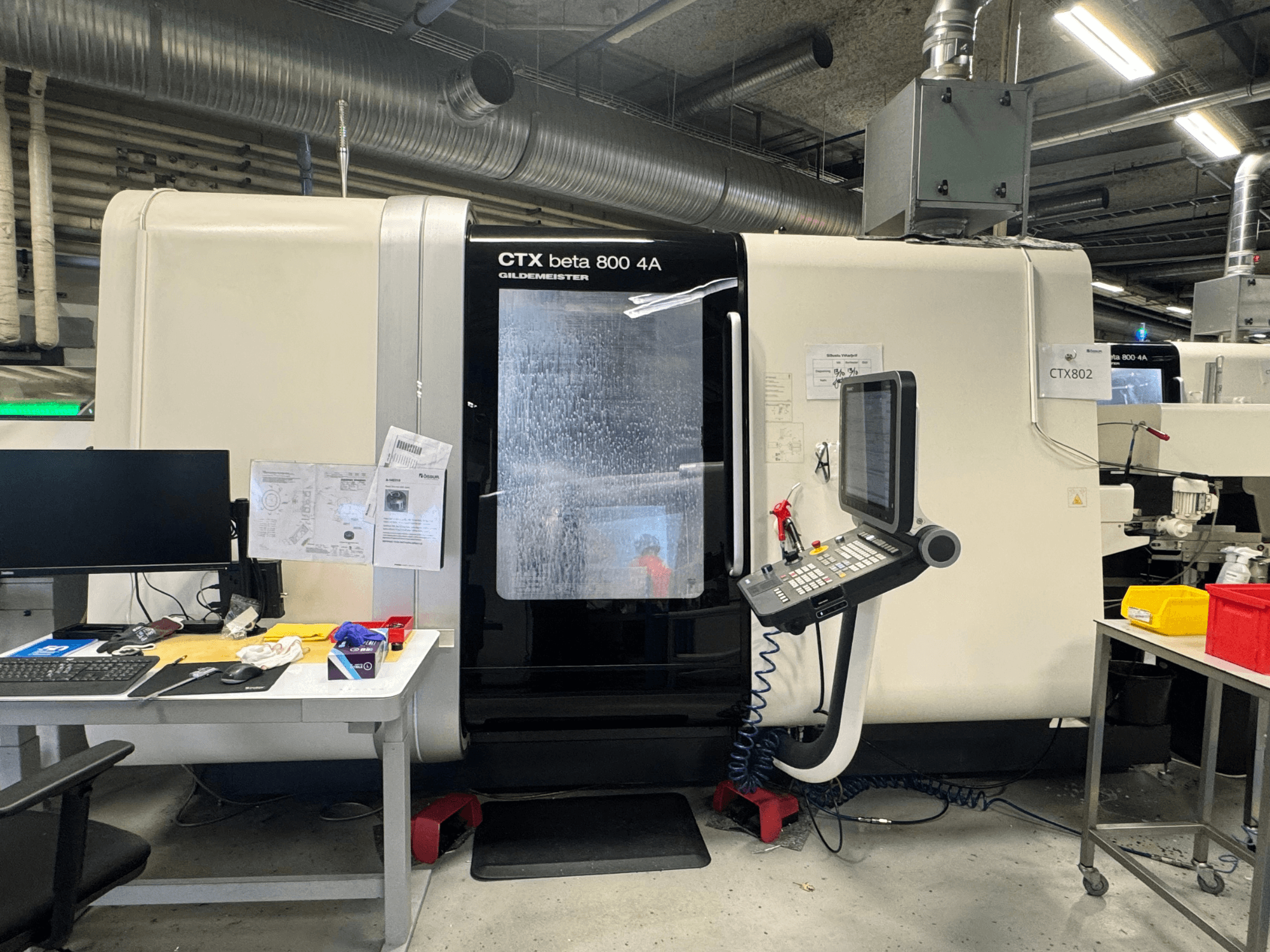 Máquina CNC CTX beta 800 4A en un taller, vista lateral que muestra el panel de control y el espacio de trabajo abarrotado de herramientas y documentos.