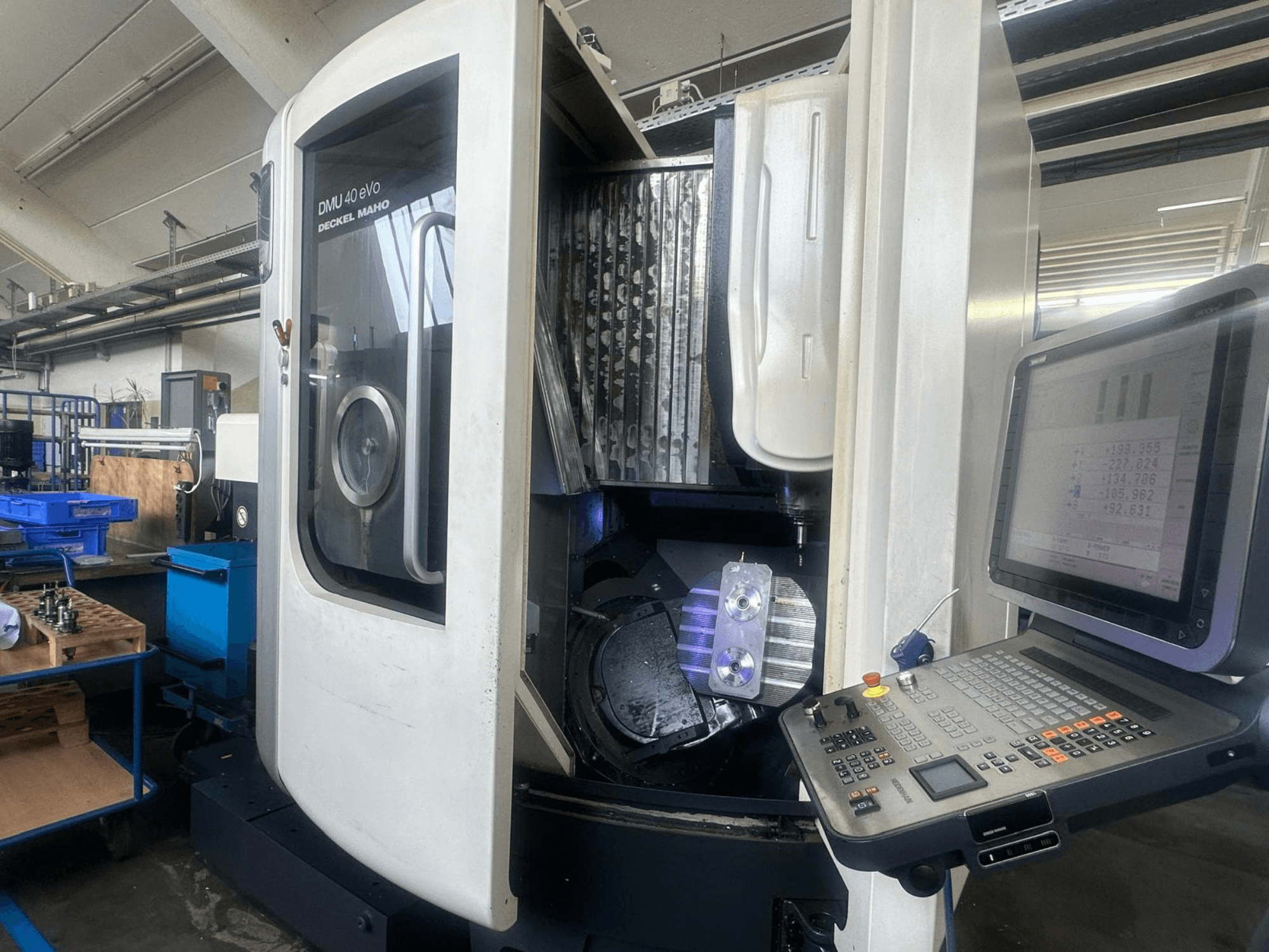 Fresadora DMU 40 eVo de Deckel Maho en un taller, vista frontal, mostrando el panel de control y la pieza metálica en el husillo.