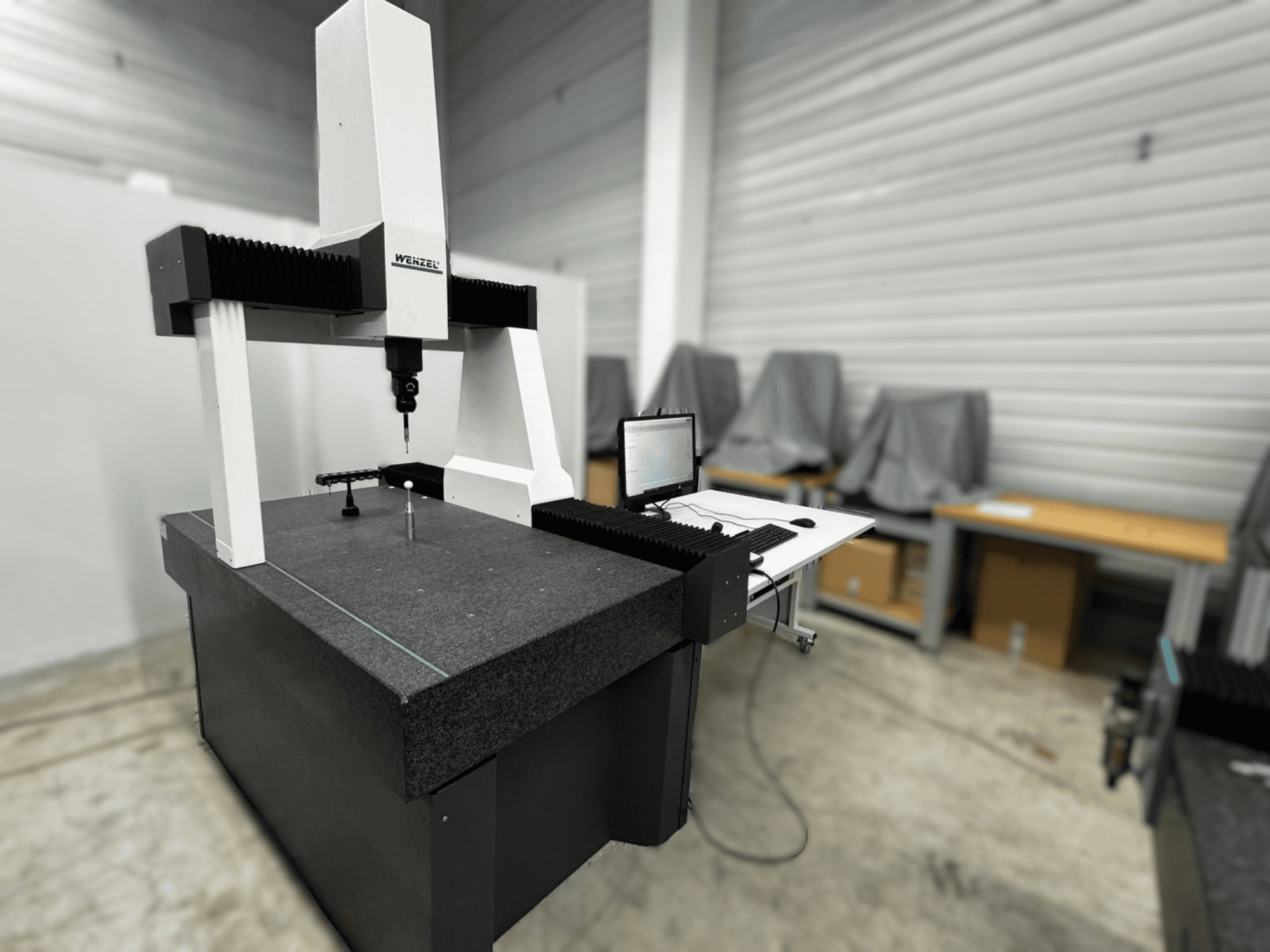 Máquina de medición por coordenadas Wenzel LH 54 en una vista lateral, con una sonda y una interfaz de ordenador sobre una base gris.