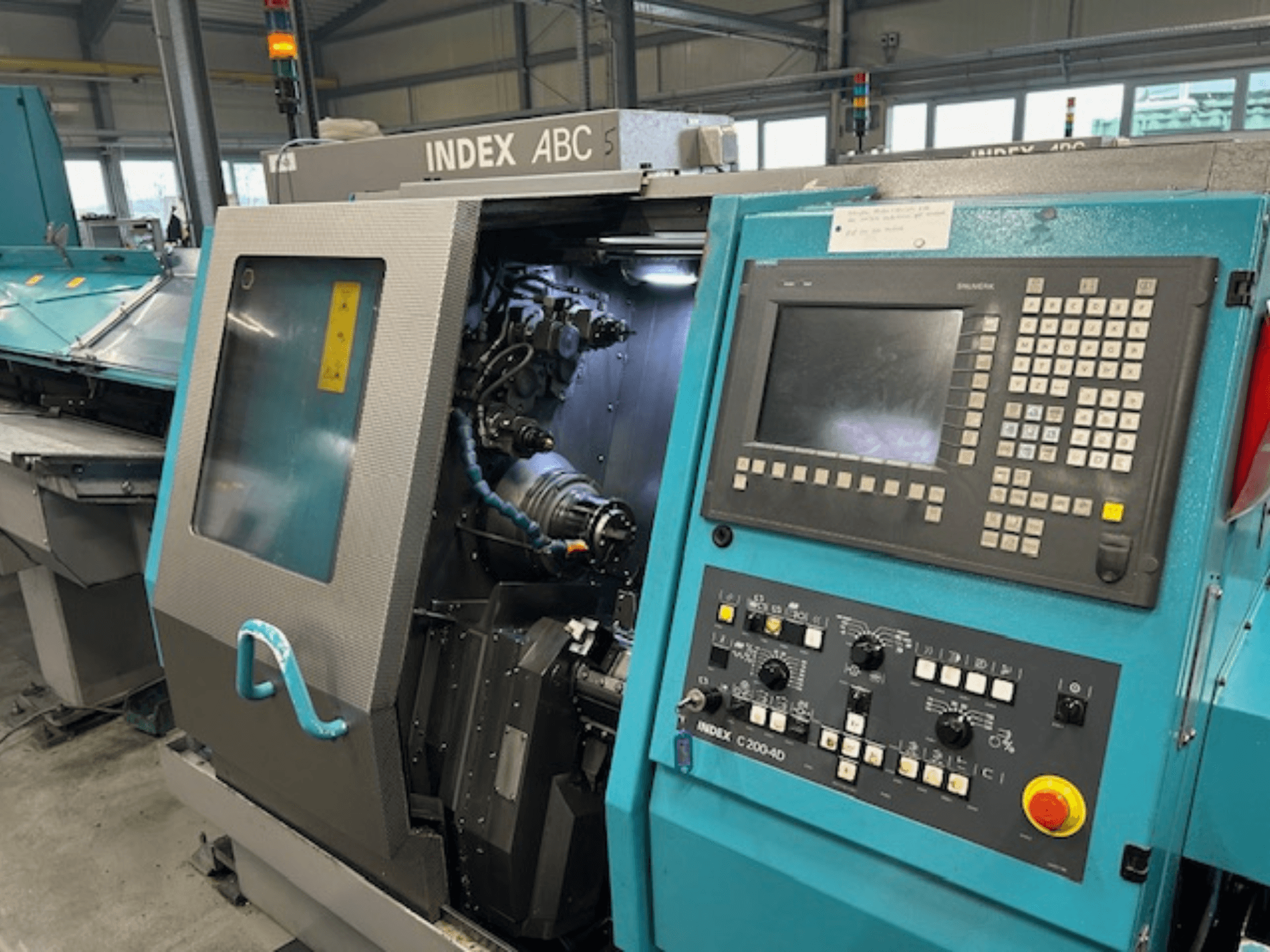 Front view of an INDEX C200-AD CNC lathe with control panel, visible internal components, and safety features.