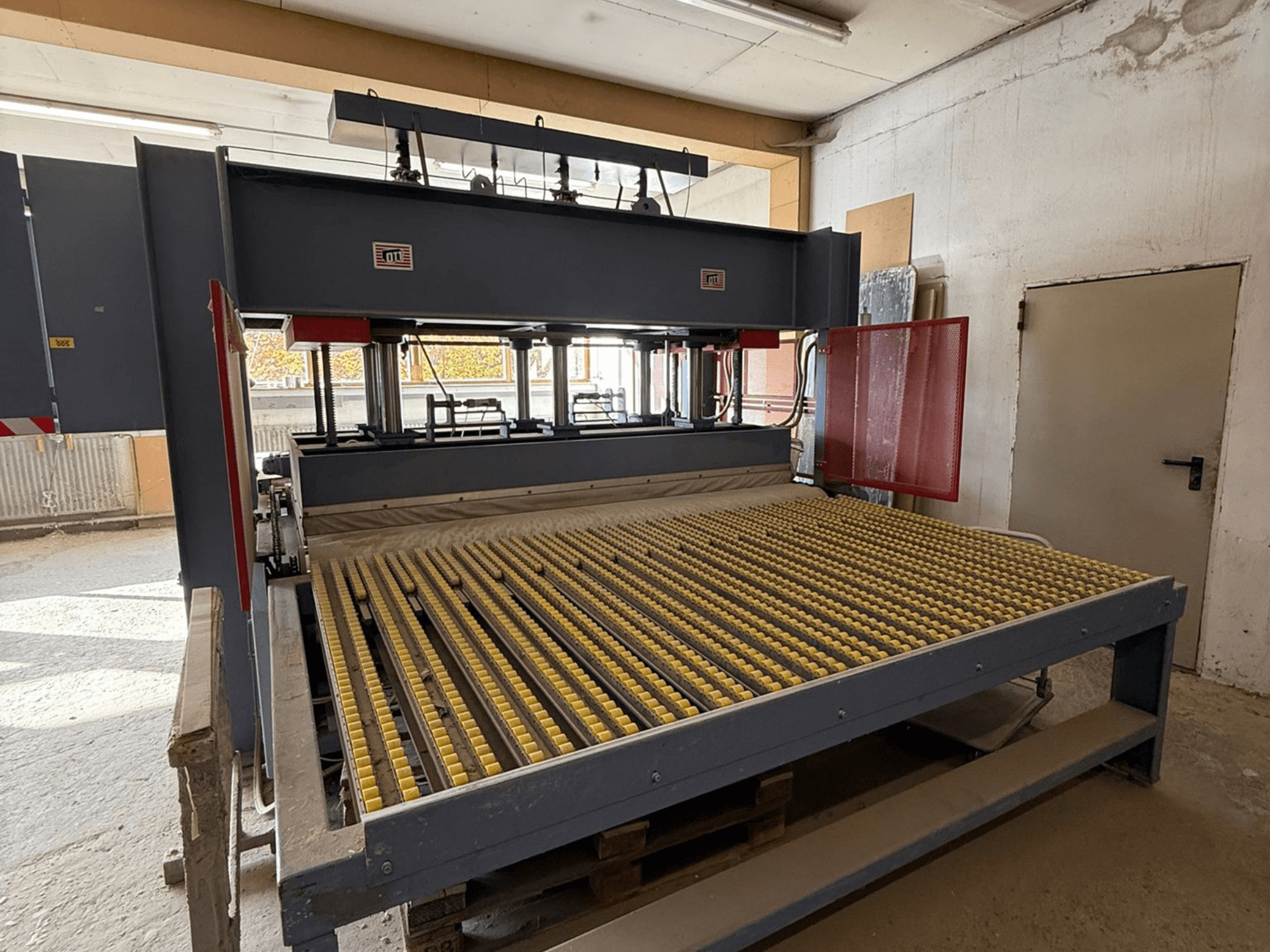 Industrial machine with yellow rollers, front view, brand logo visible, used for processing materials in a workshop setting.