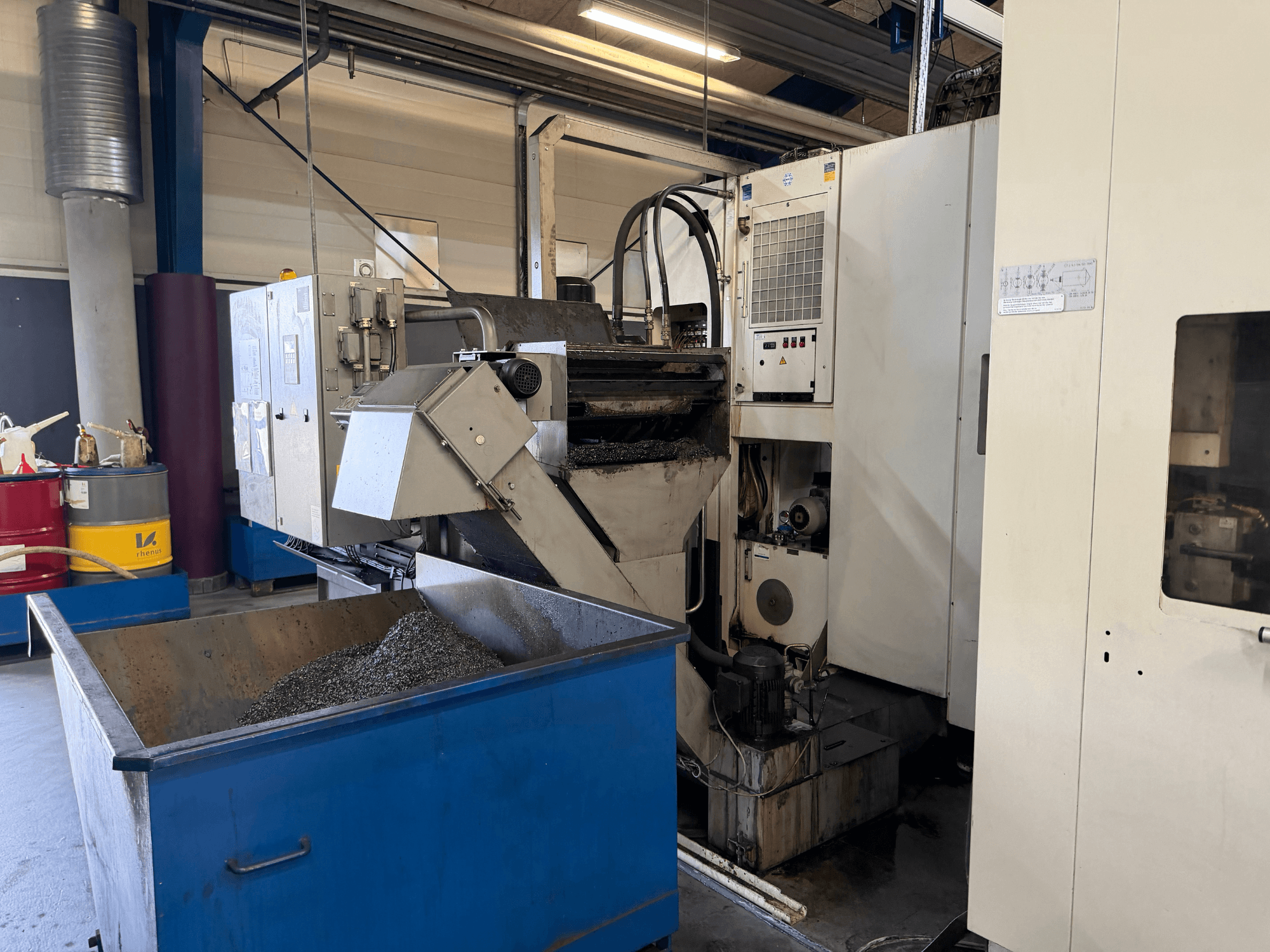 Vista frontal del centro de mecanizado horizontal HELLER MCH 250 con el recipiente de reciclaje de refrigerante metálico y el panel de control visibles.