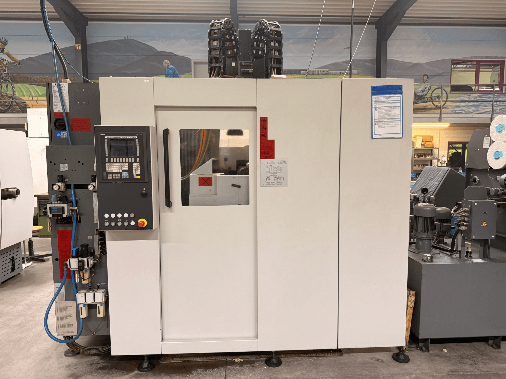 Centro de mecanizado CNC blanco con panel de control, vista frontal, con botones y pantalla digital, en un entorno de taller.