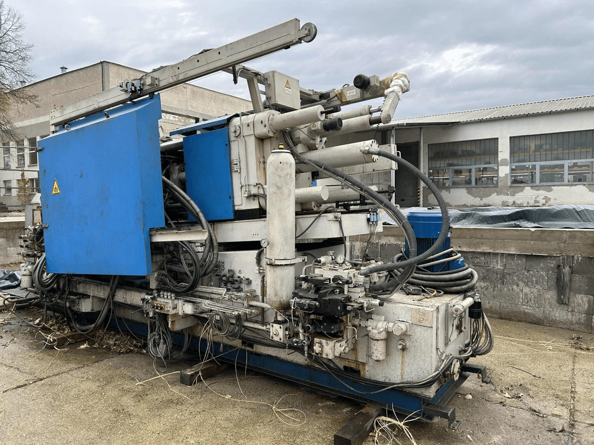 Gran máquina hidráulica industrial con carcasa azul, varias mangueras y componentes metálicos, vista de lado.