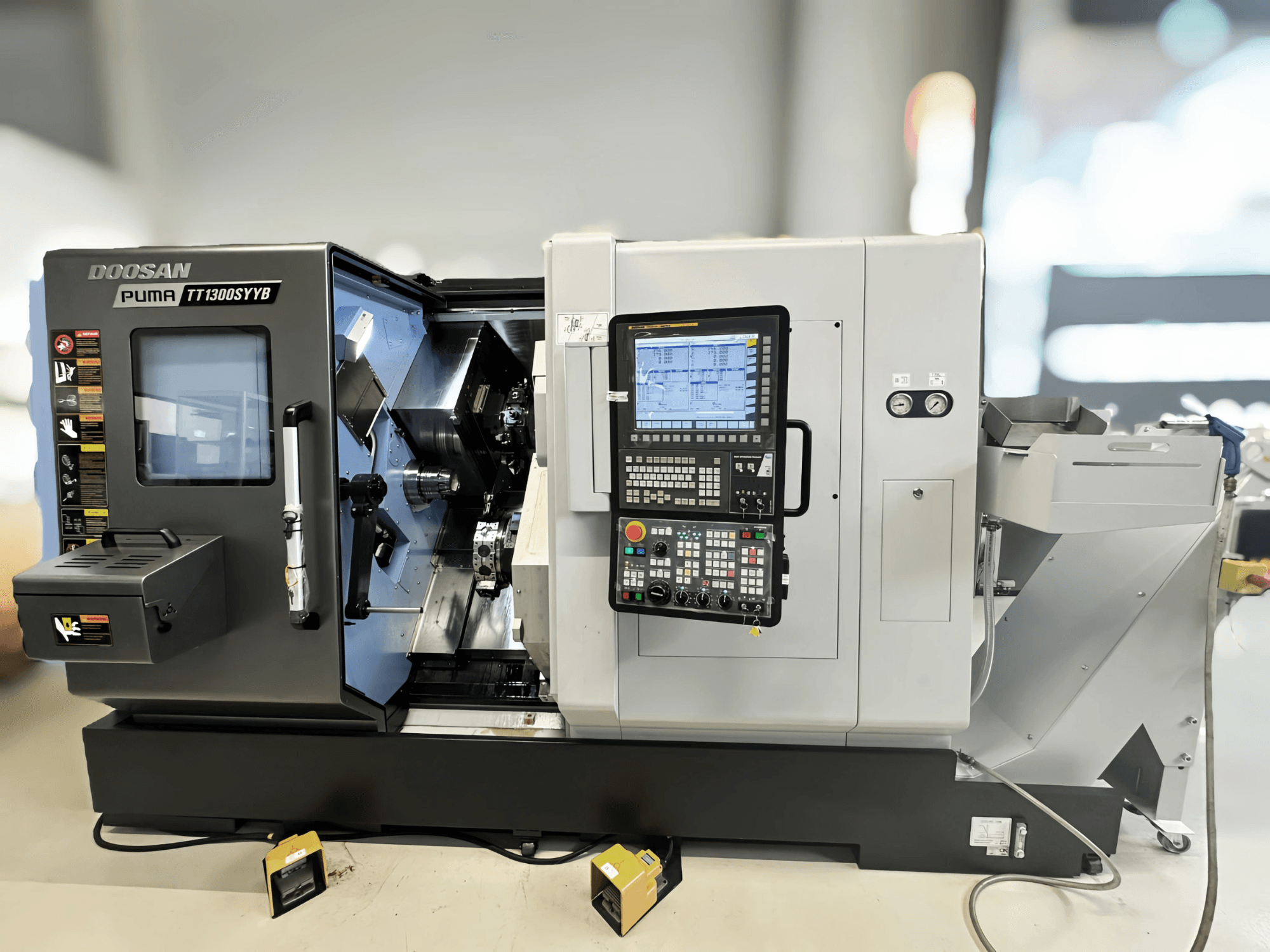 Centro de torneado y fresado Doosan Puma TT1300SYYB en vista lateral, mostrando el panel de control y el interior de la máquina con las herramientas visibles.
