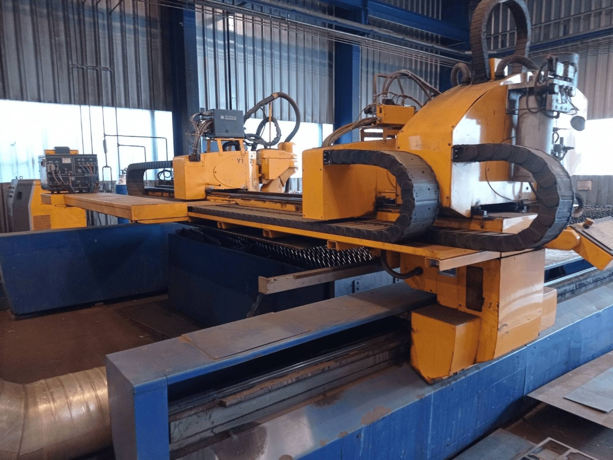 Máquina de corte por plasma CNC amarilla con dos brazos horizontales, mostrada de frente, con panel de control y bancada de corte.