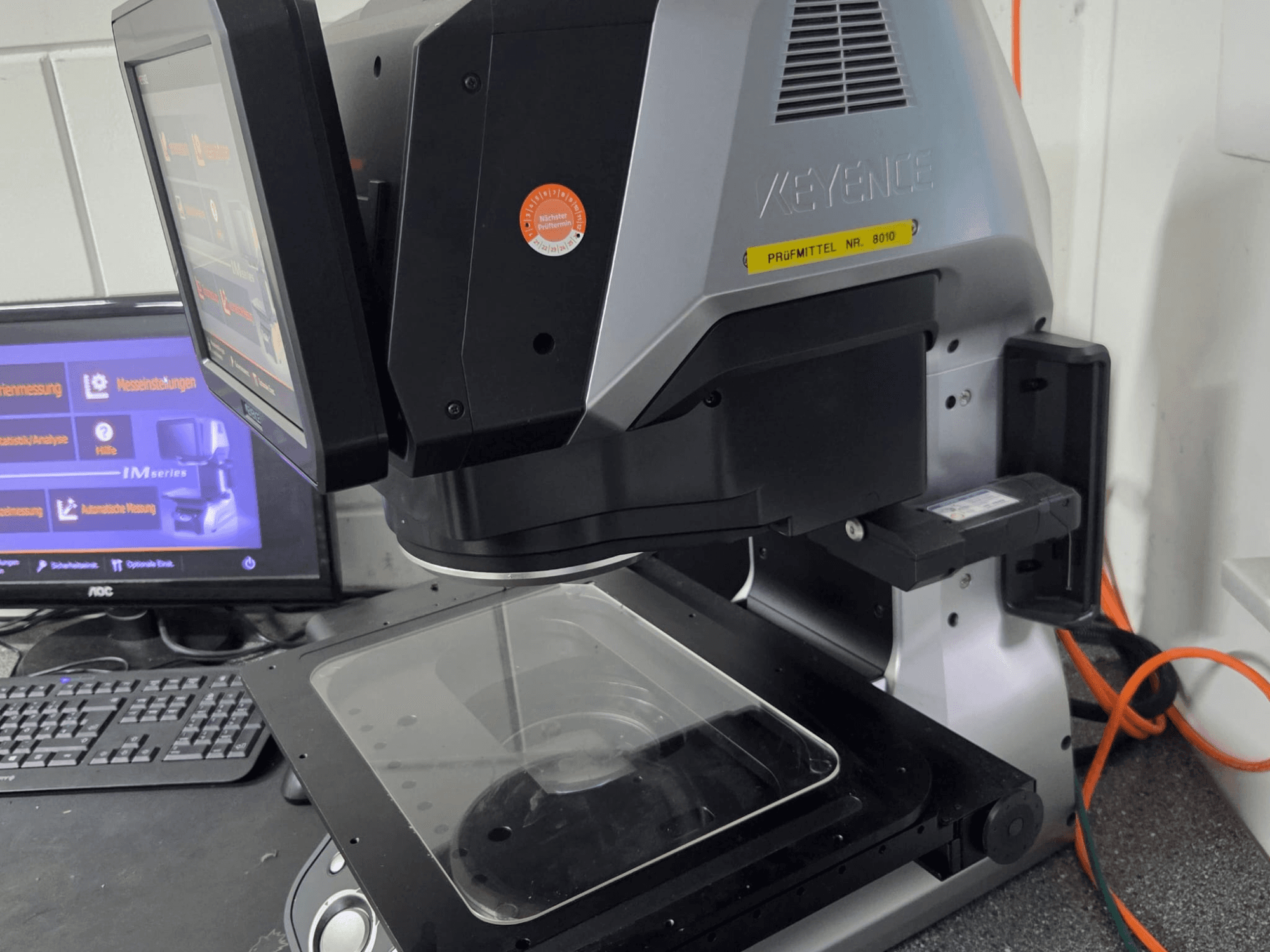 Máquina de medición óptica KEYENCE IM 7030, vista frontal con pantalla táctil y placa de medición de vidrio.