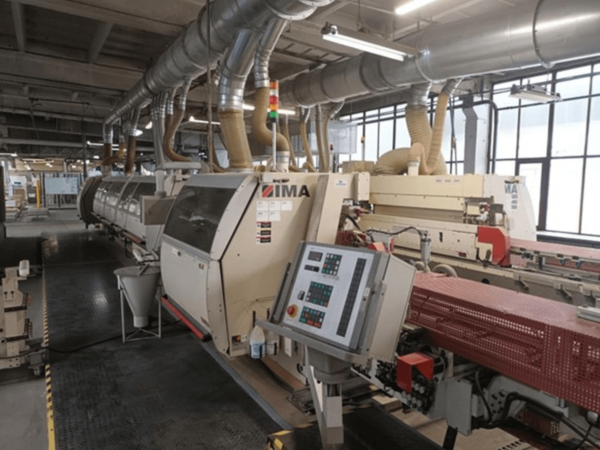 Maquinaria industrial IMA en una fábrica, vista frontal, con paneles de control y tubos de extracción de polvo.