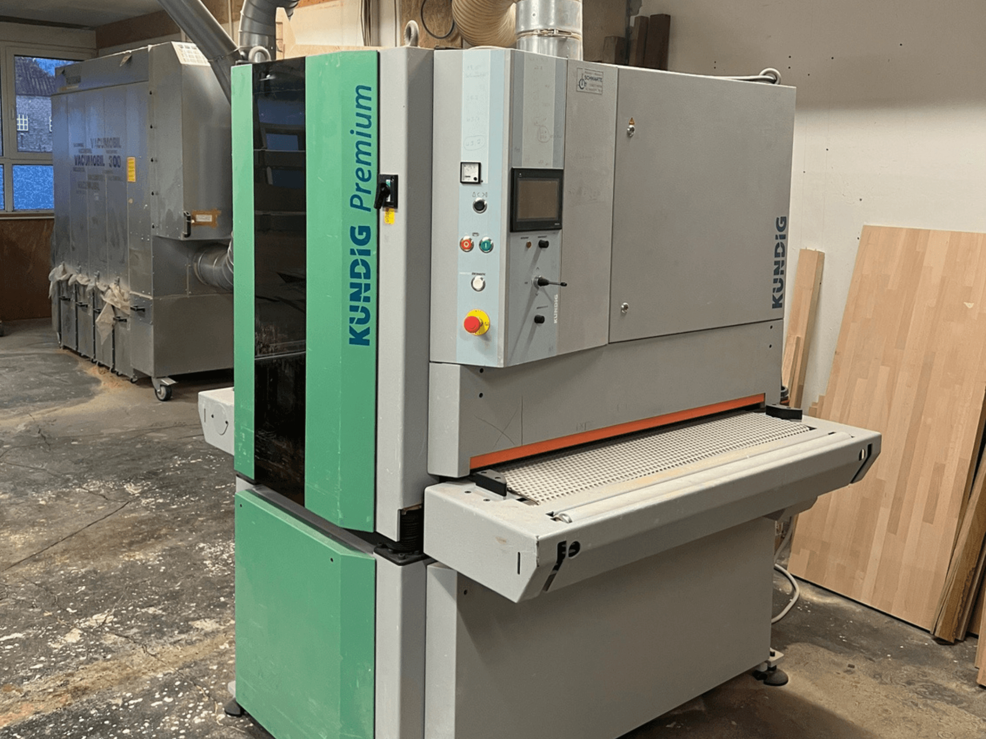 Lijadora de banda Kundig Premium-1 1100K en gris y verde, mostrada en una vista lateral con el panel de control y la banda de lijado visibles.